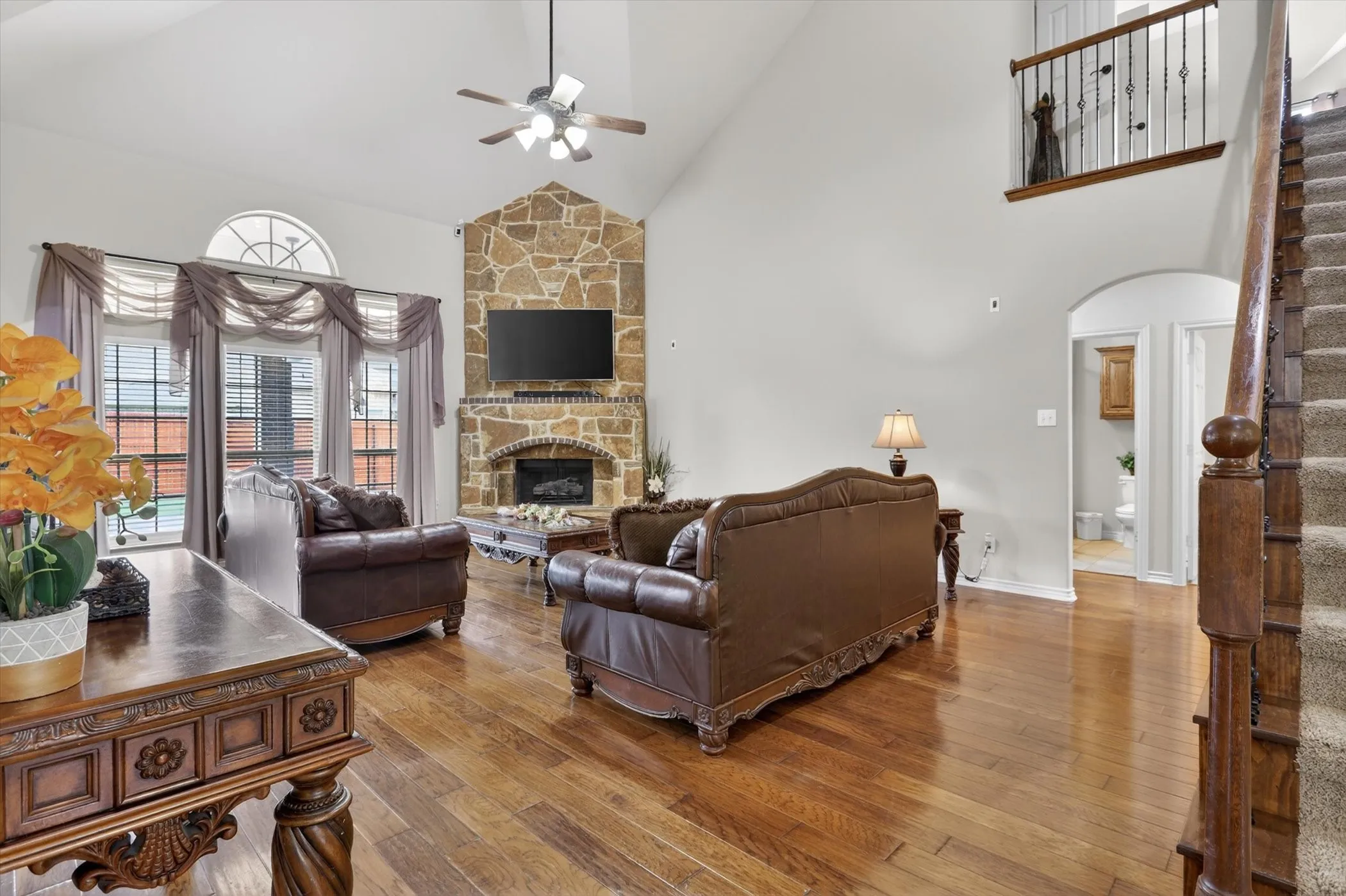 Vaulted living area featuring wood flooring, a stone gas start fireplace and beautiful windows