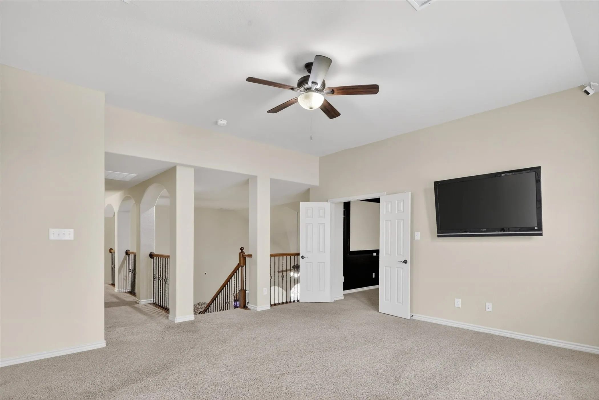 Carpeted room featuring a ceiling fan with integrated lighting, a wall-mounted television, and a doorway with bifold doors