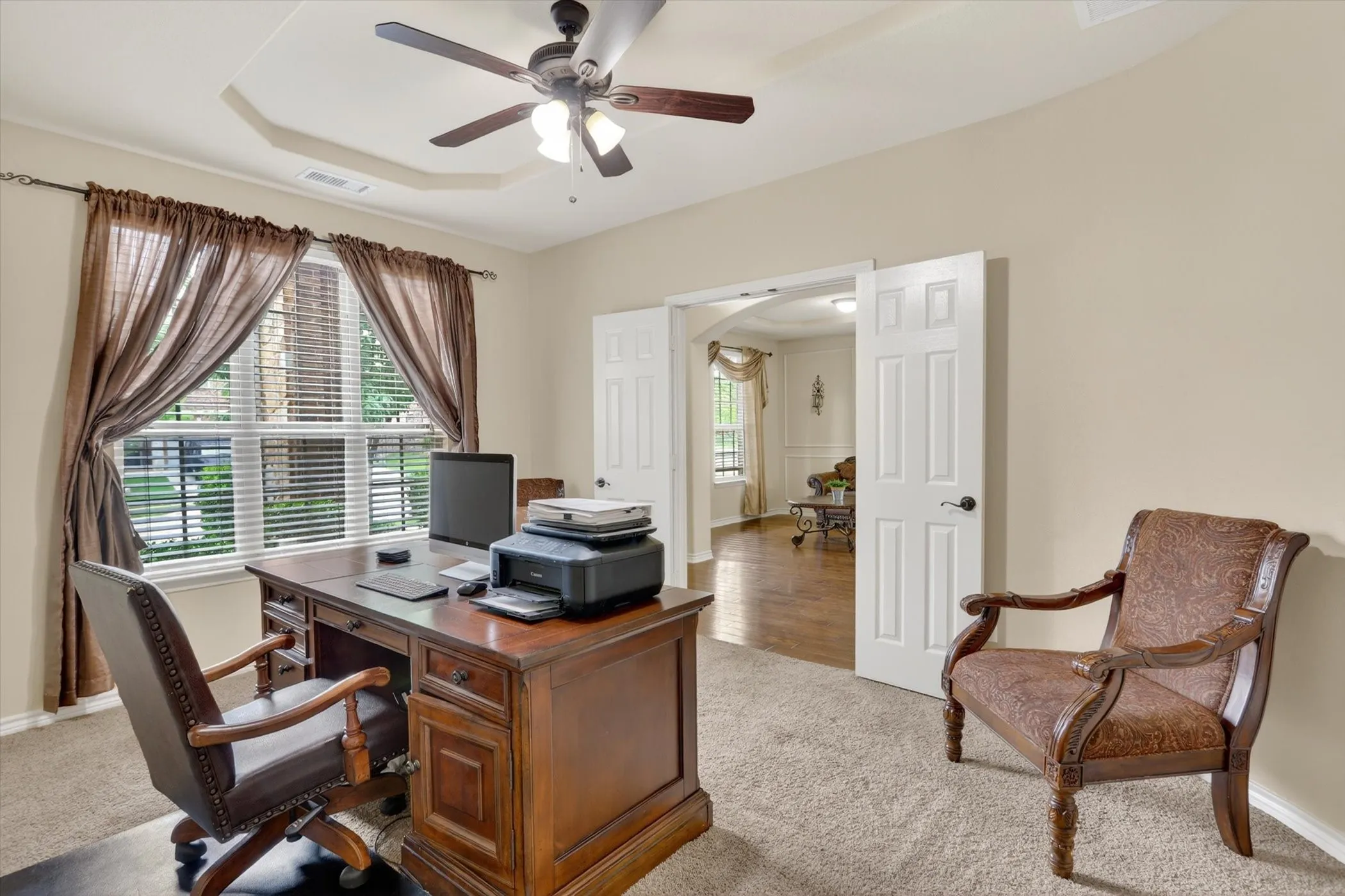 Room featuring a double window with blinds, a tray ceiling, and a ceiling fan