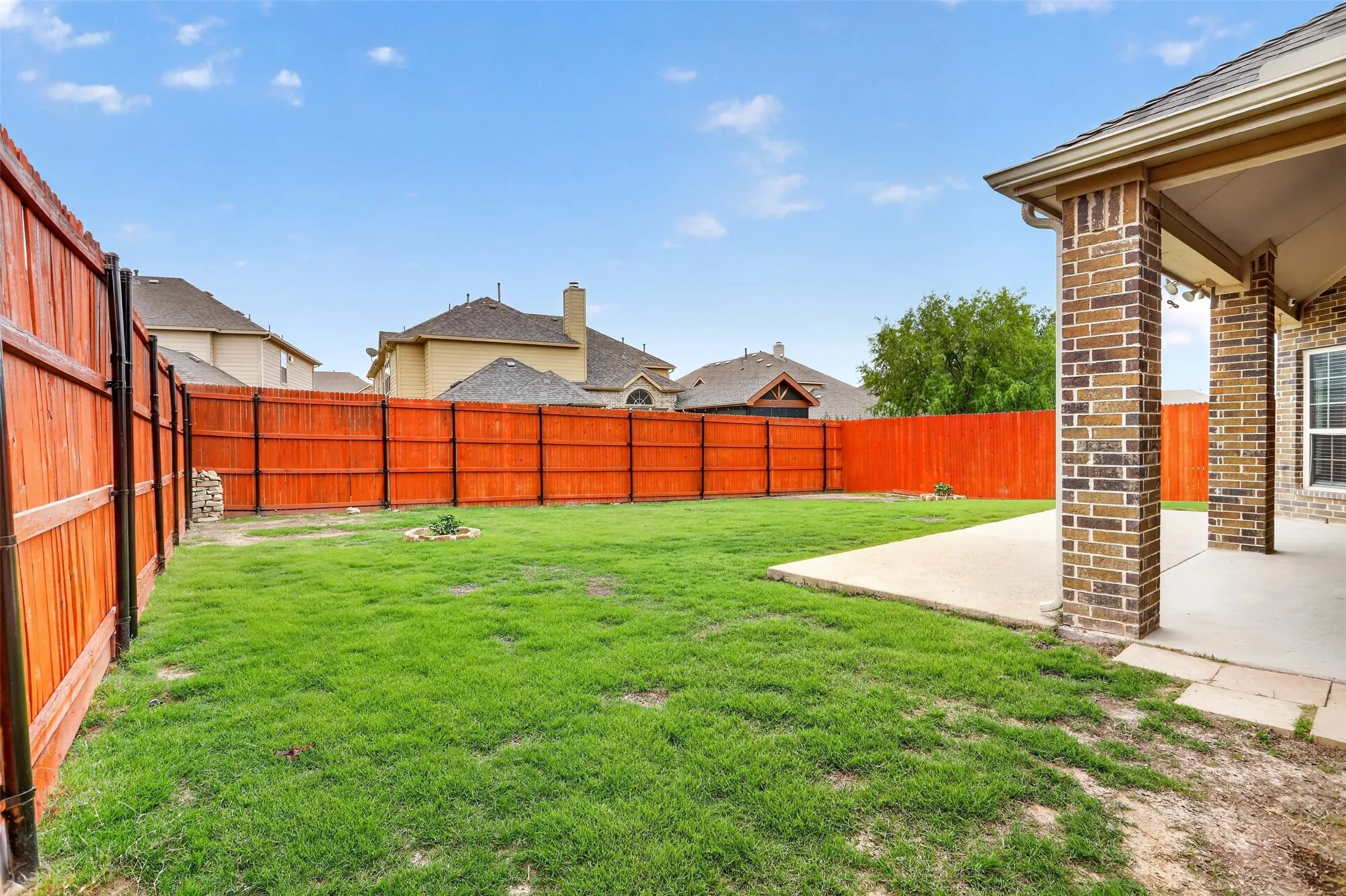 Expansive backyard featuring a manicured lawn, full wood fencing, a brick-columned covered patio, and a concrete patio surface