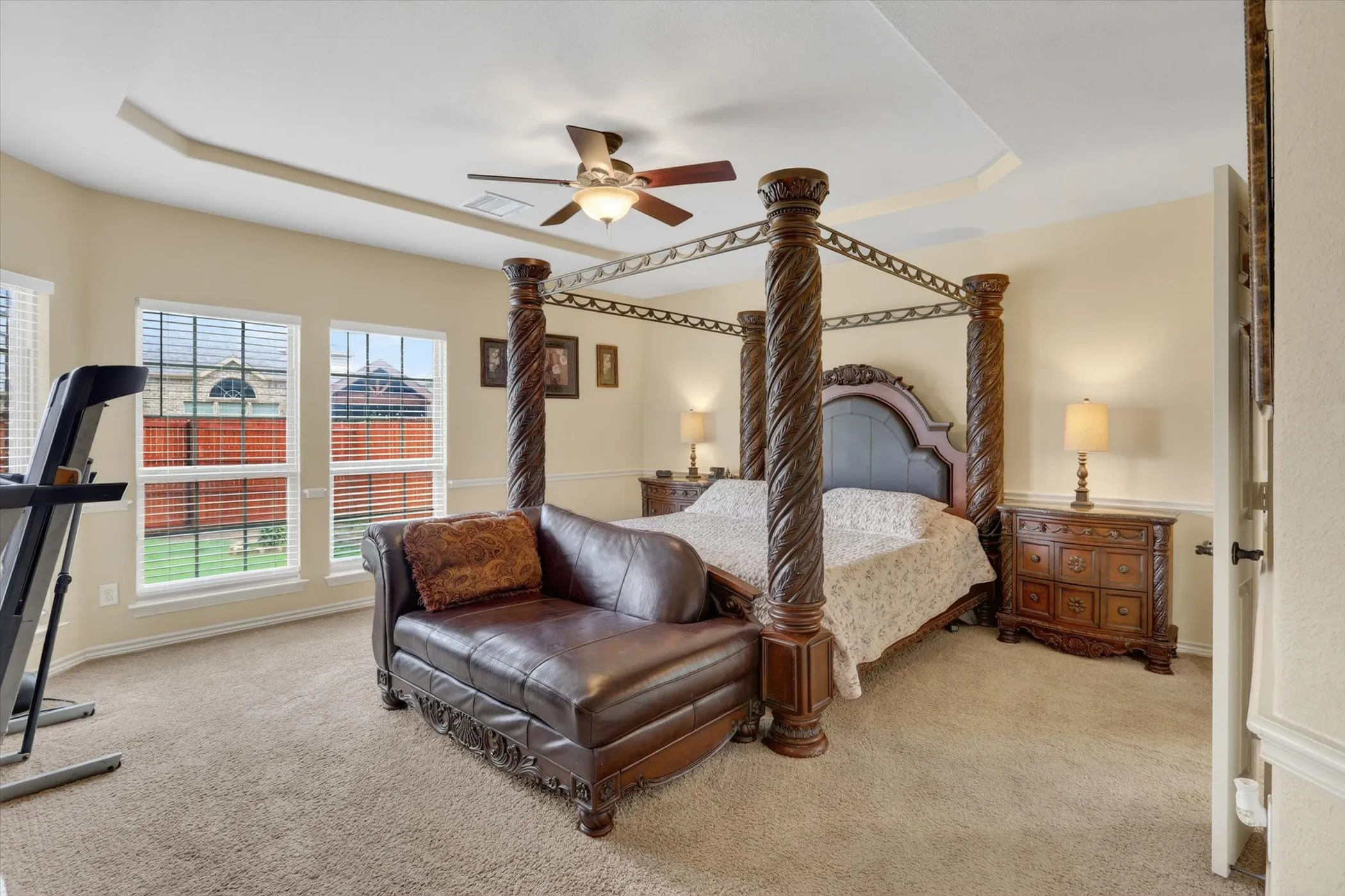 Carpeted bedroom featuring a tray ceiling, ceiling fan with integrated lighting, multiple windows with blinds, and white trim molding