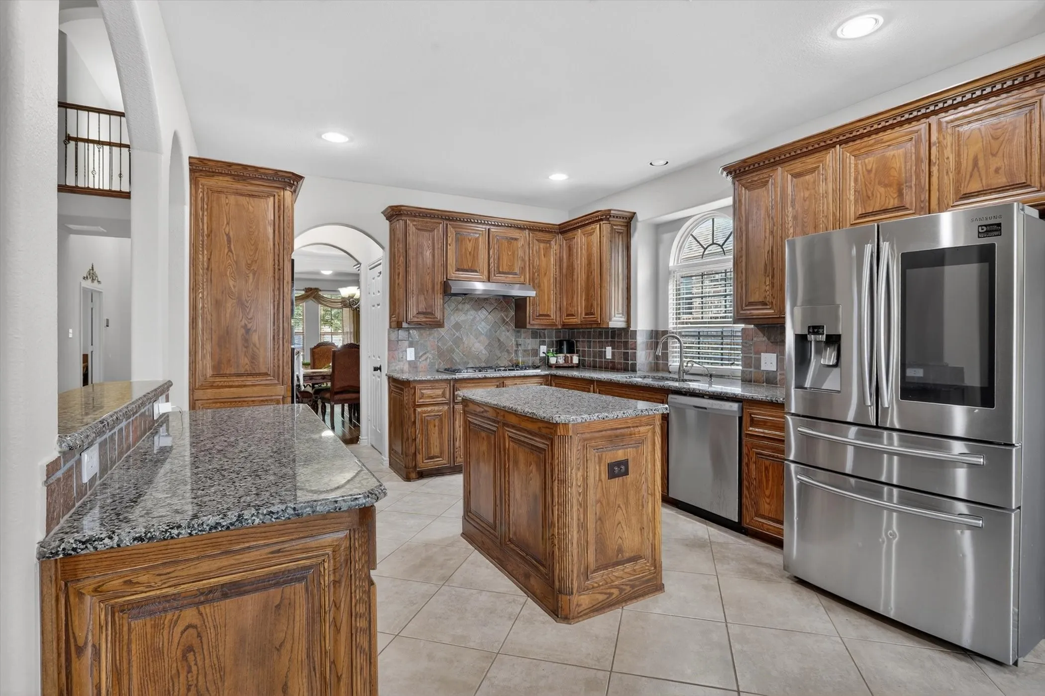 Kitchen featuring wood cabinetry, 5 burner gas stove, double ovens, granite countertops, stainless steel appliances, a center island, and tile flooring