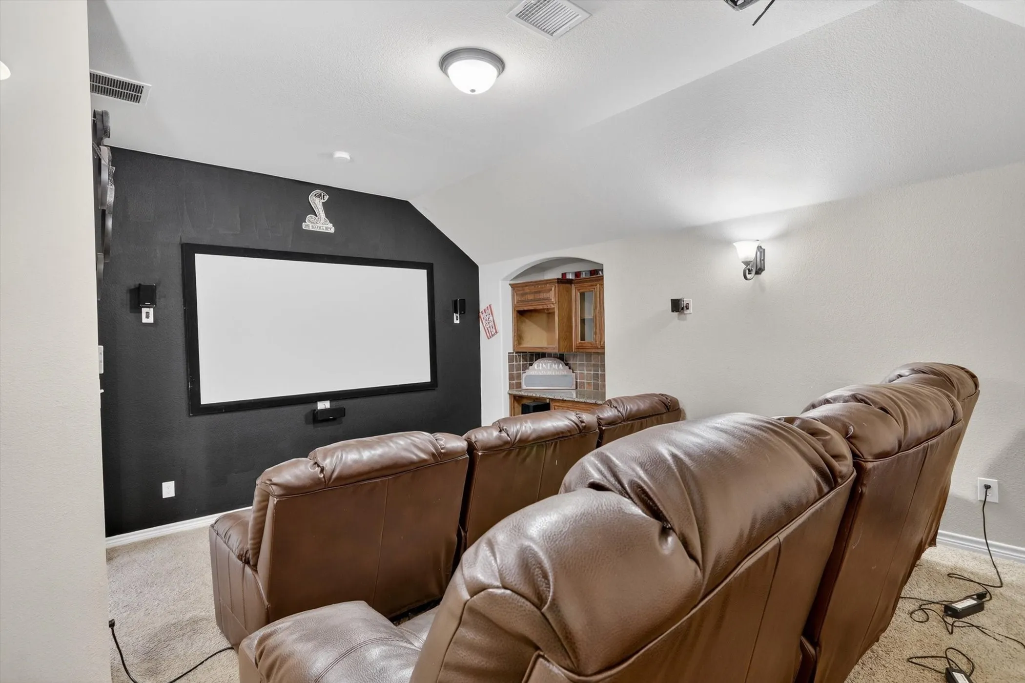 Media room featuring a large projection screen, dark accent wall, recessed lighting, and a built-in wet bar with wood cabinetry and tile backsplash