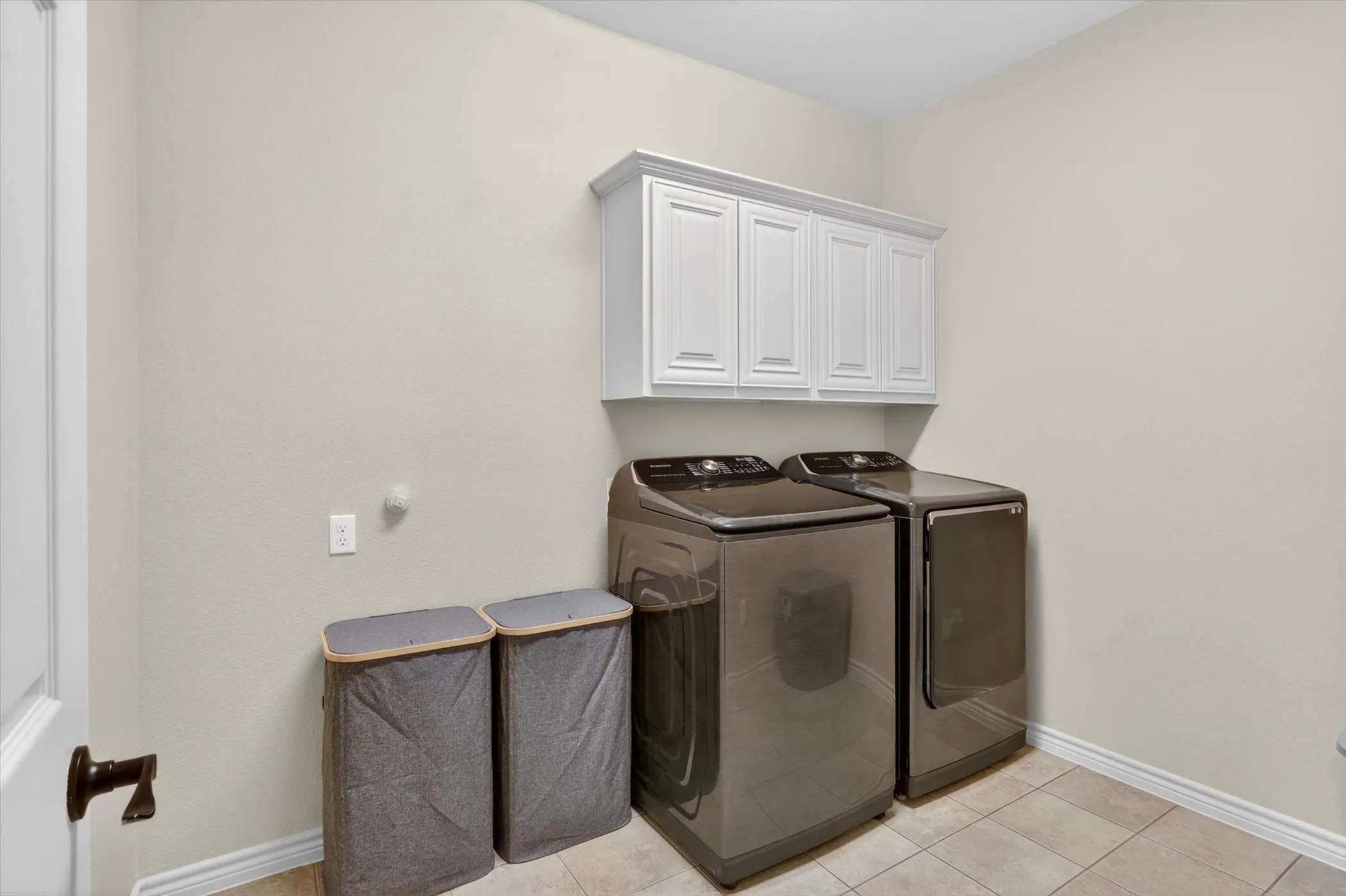 Downstairs laundry area featuring tiled flooring, white baseboards, and overhead white cabinetry
