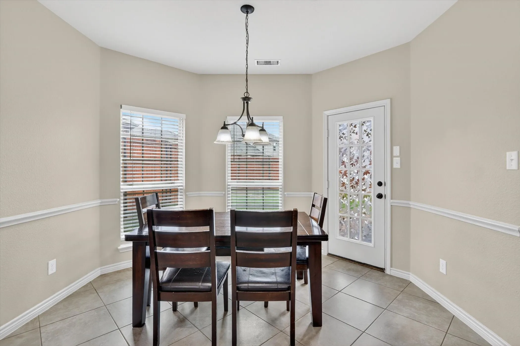 Dining area featuring tiled flooring, wainscoting, an overhead chandelier, and a glass-paneled door