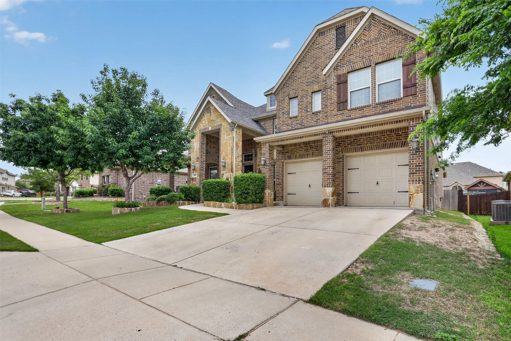 Brick and stone exterior with a covered entry, two-car garage, concrete driveway, and manicured landscaping