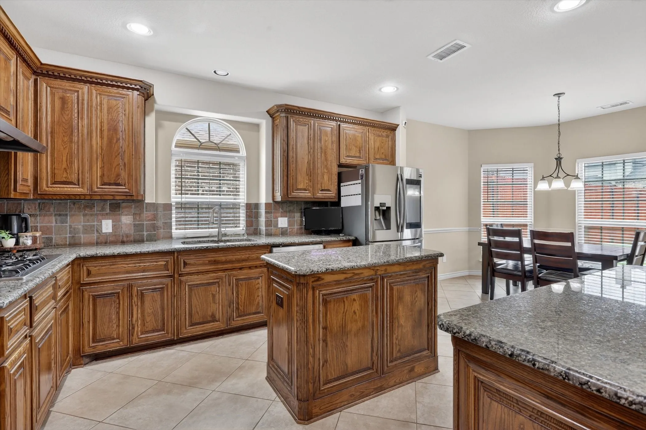 Kitchen featuring wood cabinetry, granite countertops, tile flooring, a central island, and an arched window above the sink