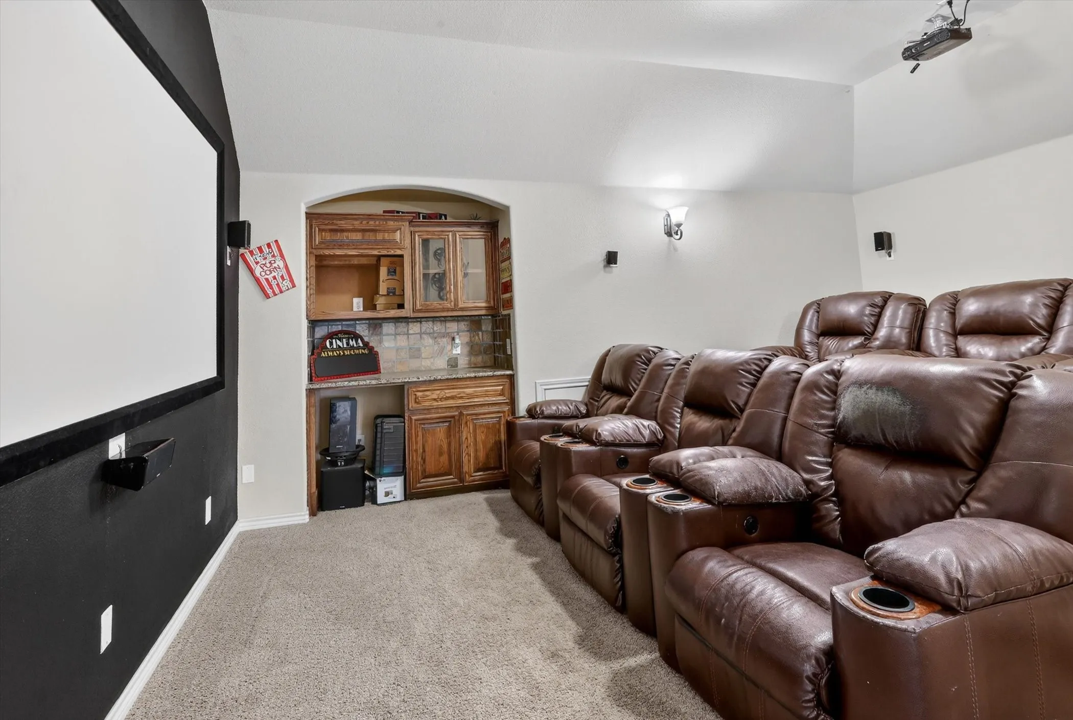 Dedicated media room featuring a large projector screen, built-in dry bar, wood-finish cabinetry, and recessed lighting