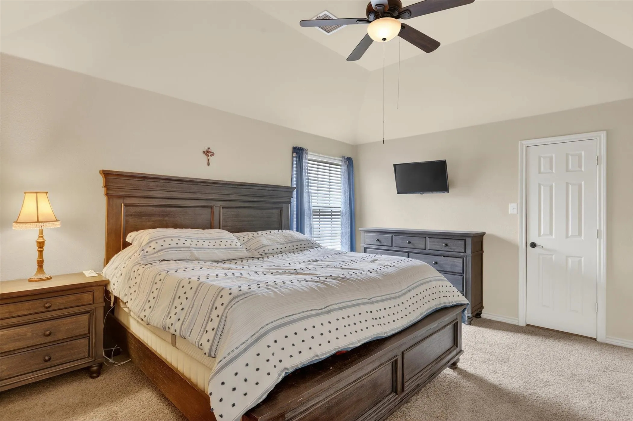 Spacious bedroom with vaulted ceilings, neutral-toned walls, and plush carpet flooring