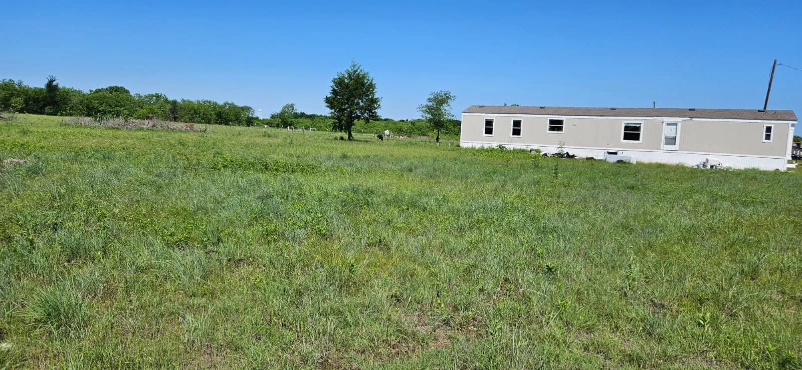 Expansive grass-covered land featuring a single-story structure with light-colored siding and multiple windows