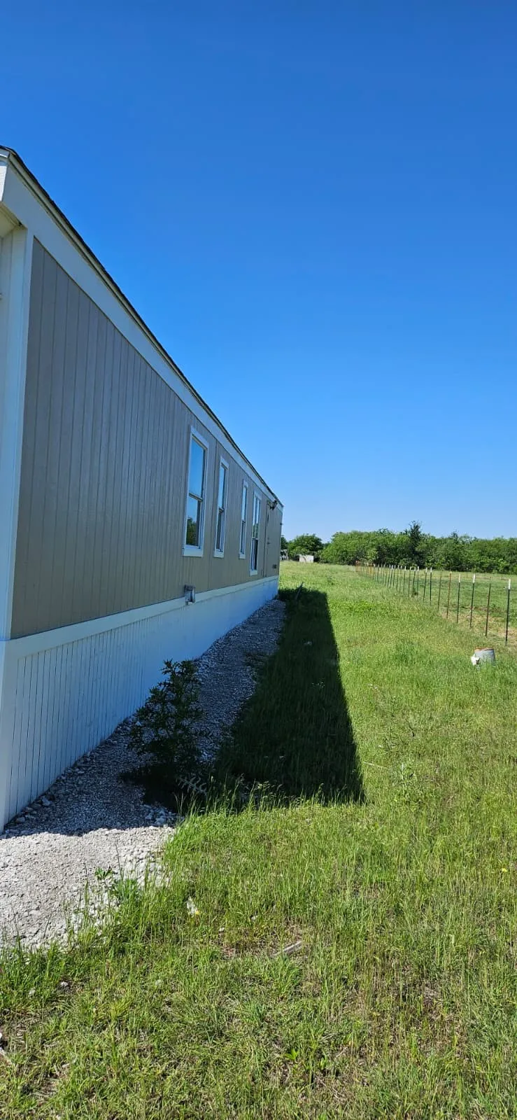 Exterior siding in a neutral tone with multiple windows, a white skirting, and a gravel perimeter