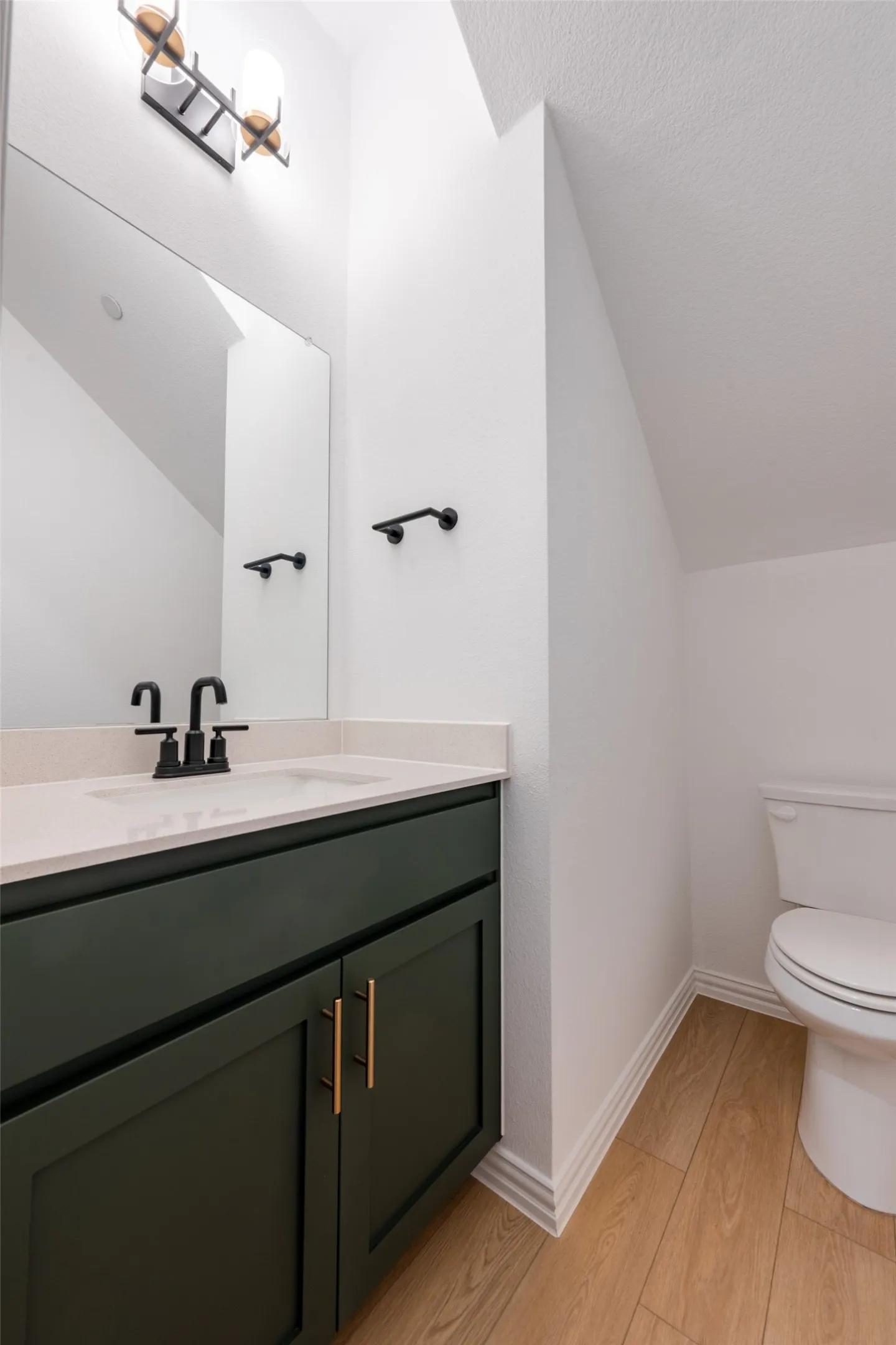 First Floor Half Bathroom featuring a dark green vanity with gold-tone hardware, a light-toned countertop, and a rectangular sink with a matte black fixtures.