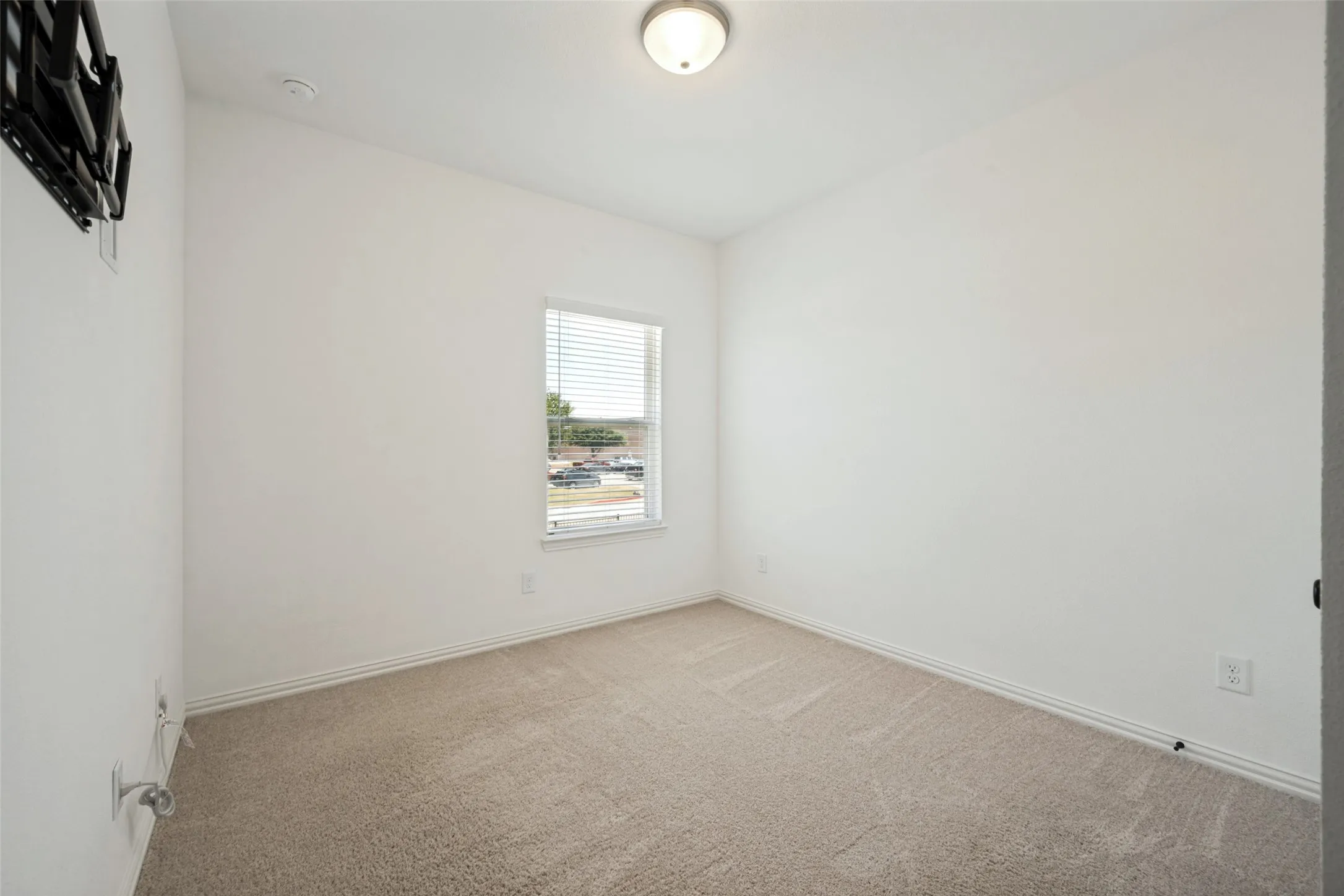 Bright secondary bedroom featuring neutral carpet flooring, a single window with blinds allowing natural light, and clean white walls
