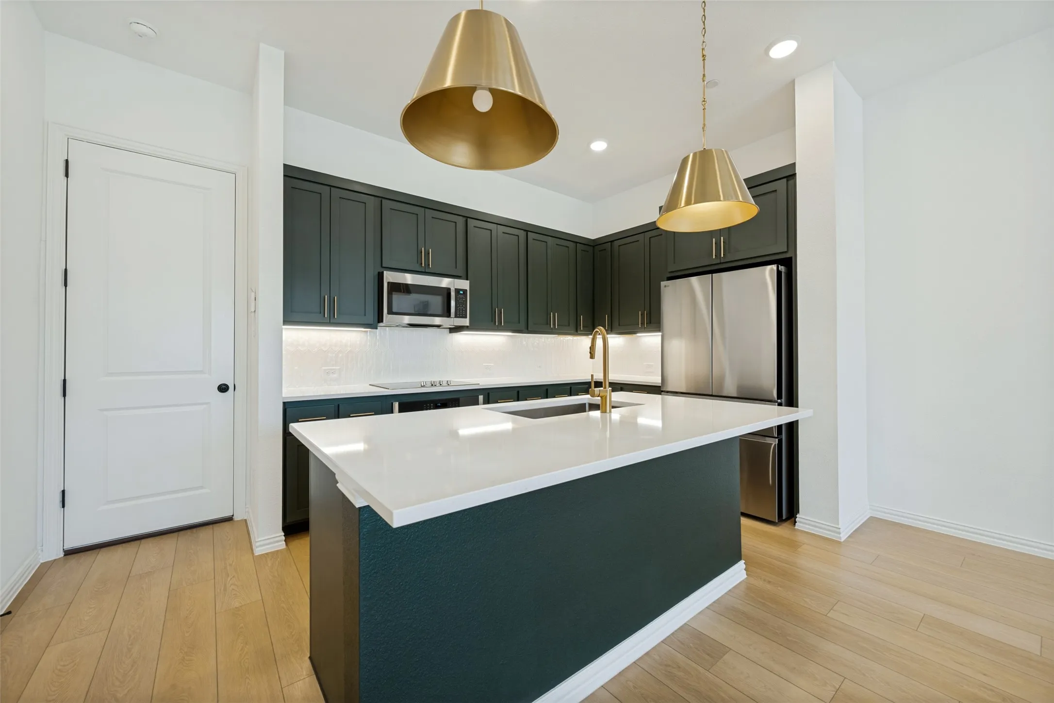 Modern kitchen featuring dark cabinetry, stainless steel appliances, and a central island with a white countertop. Refrigerator Included.