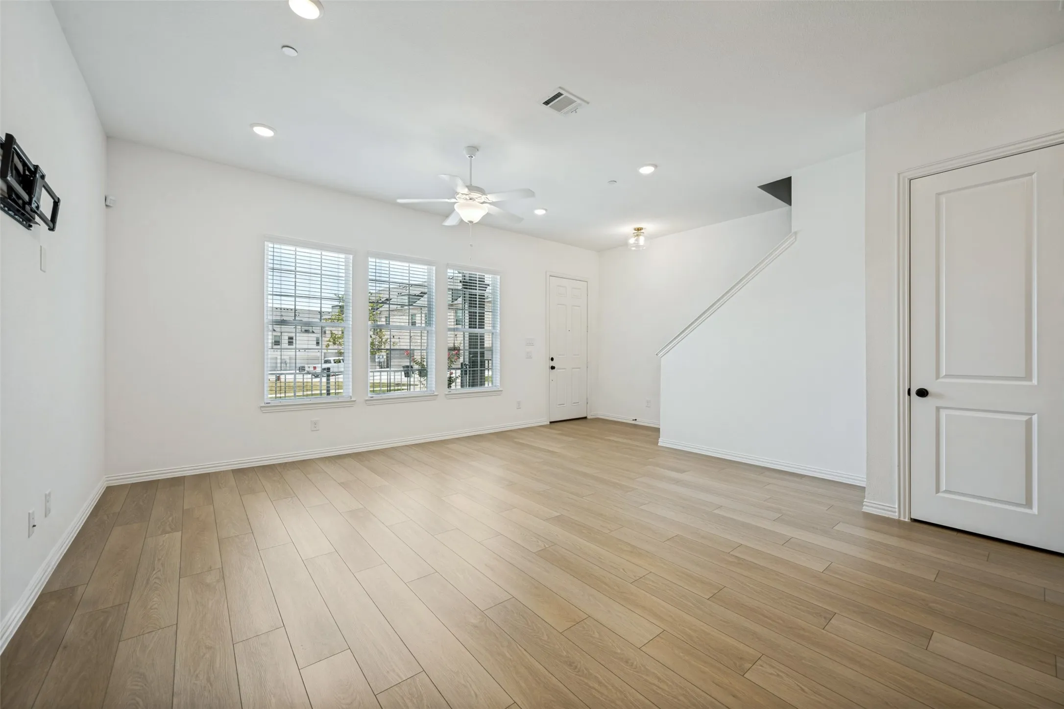 Bright, open living space showcasing gleaming wood-finish flooring throughout, recessed ceiling lighting, and a ceiling fan