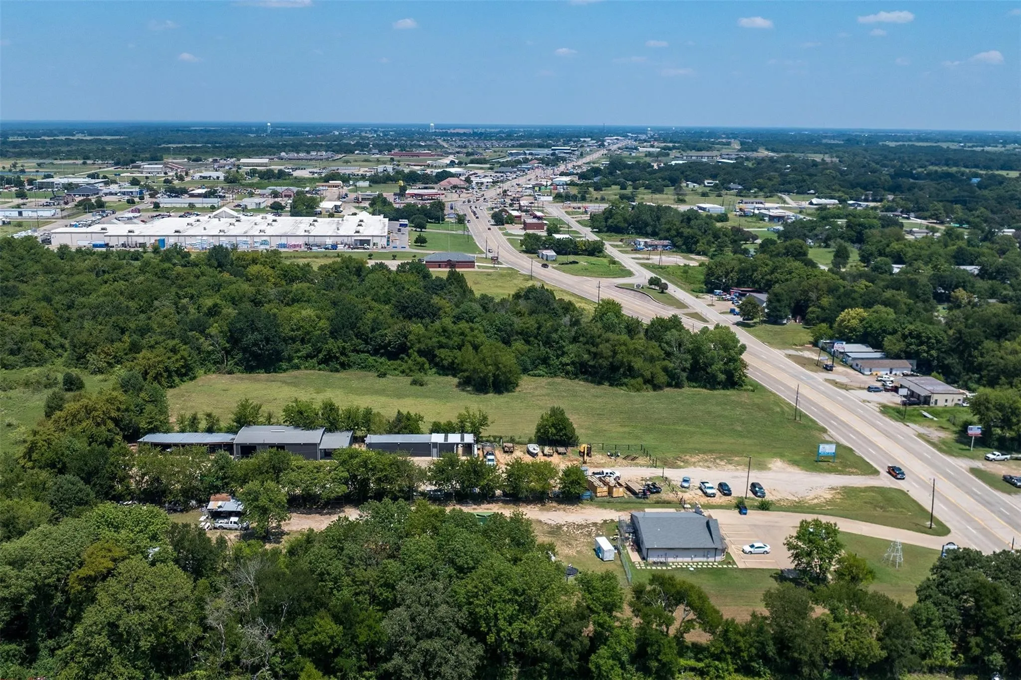 Expansive land parcel featuring multiple structures, paved road frontage, surrounding green spaces, and proximity to commercial properties