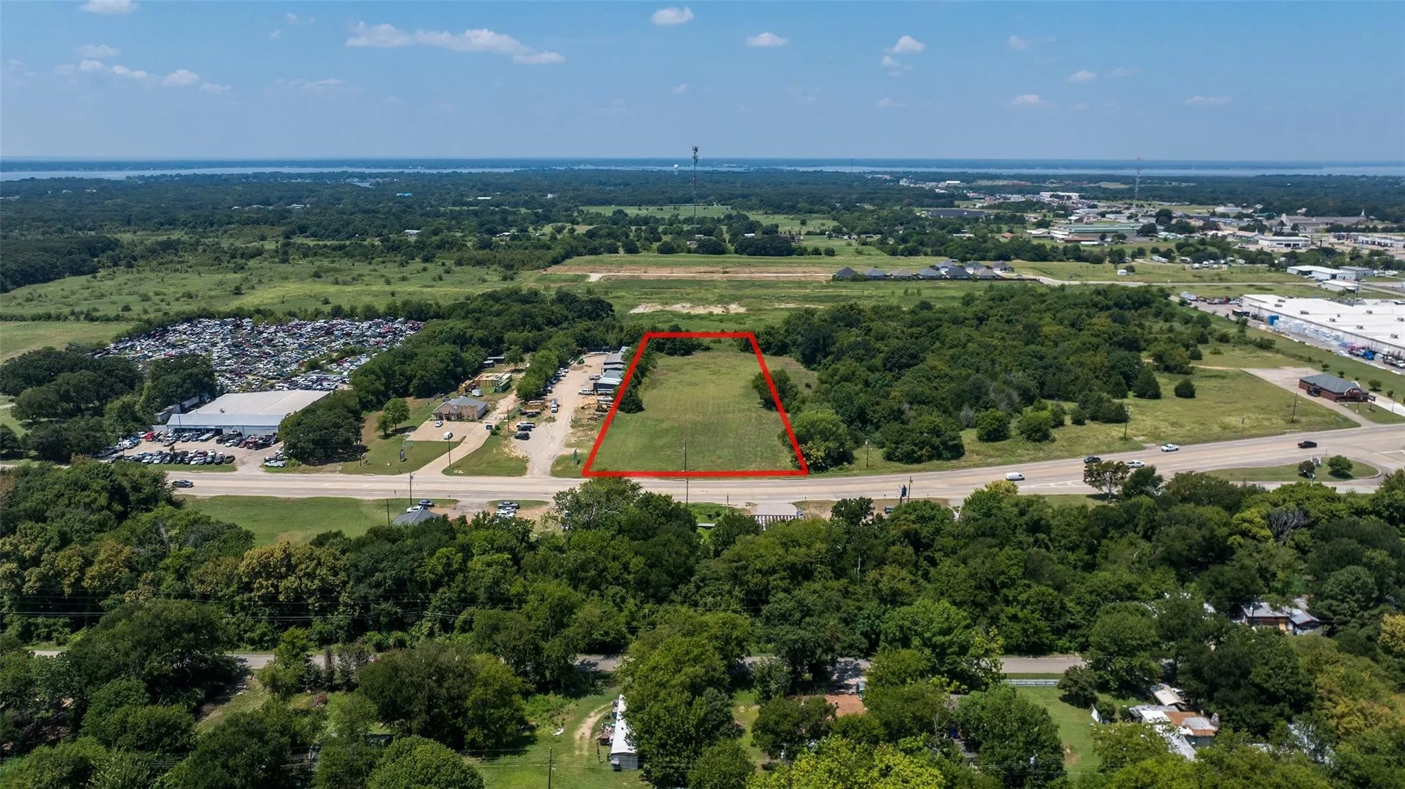 Expansive green lot bordered by mature trees and a paved road, featuring a clear boundary line