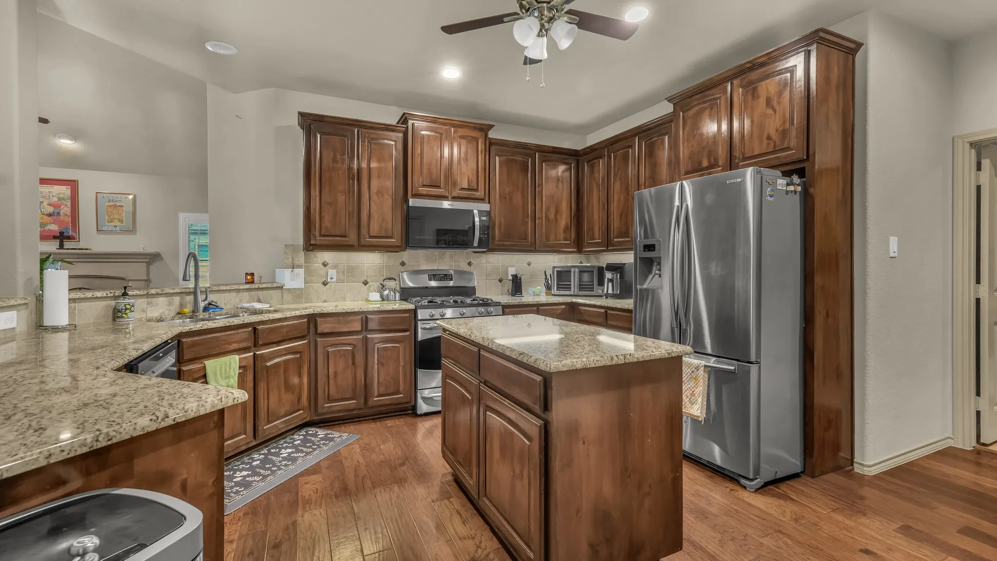 Kitchen featuring wood-finish flooring, granite countertops, wood cabinetry, a stainless steel gas range, and a central island