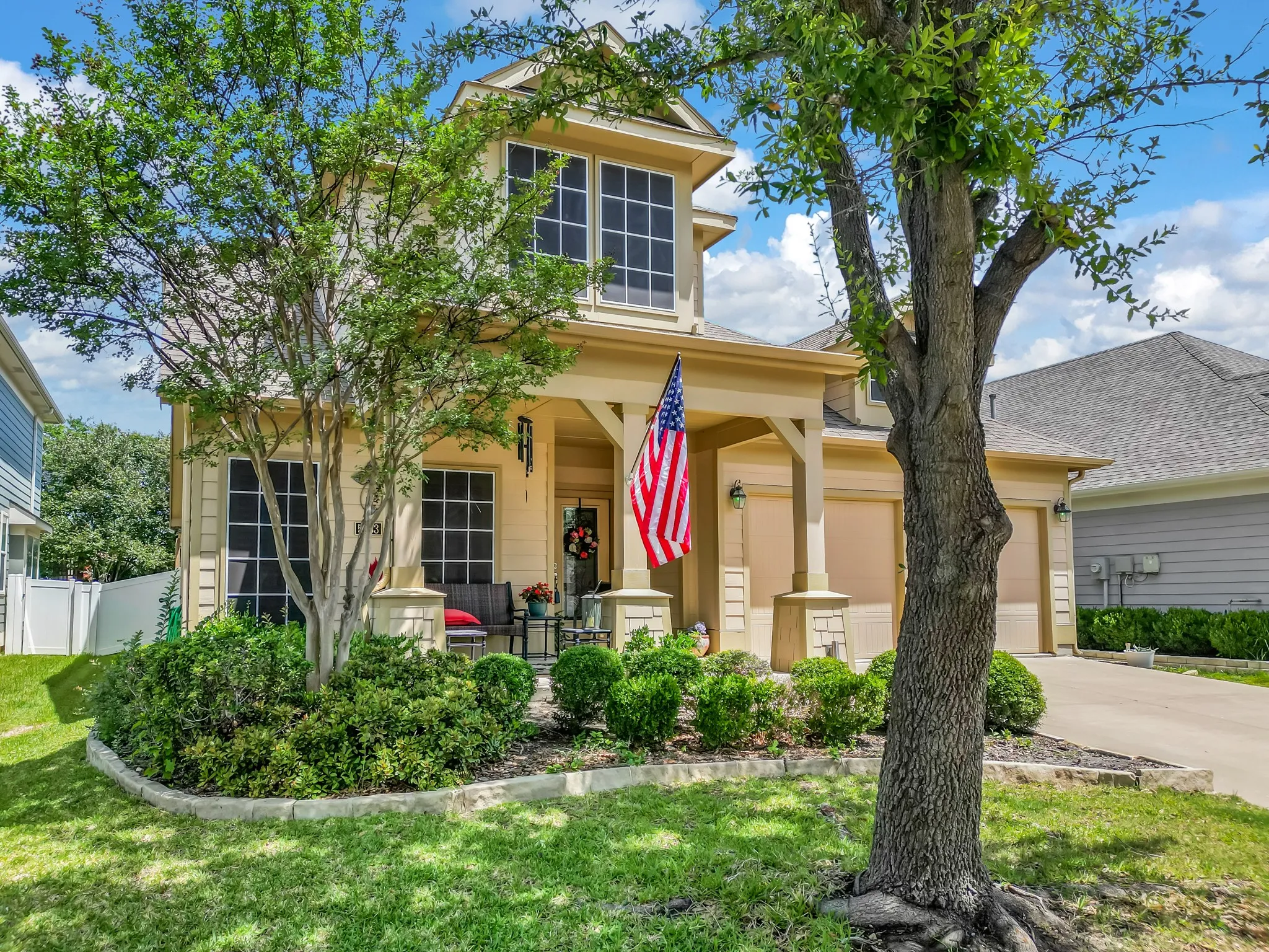 Two-story residence featuring a covered front porch, a two-car garage, and a manicured front lawn with mature trees and established landscaping