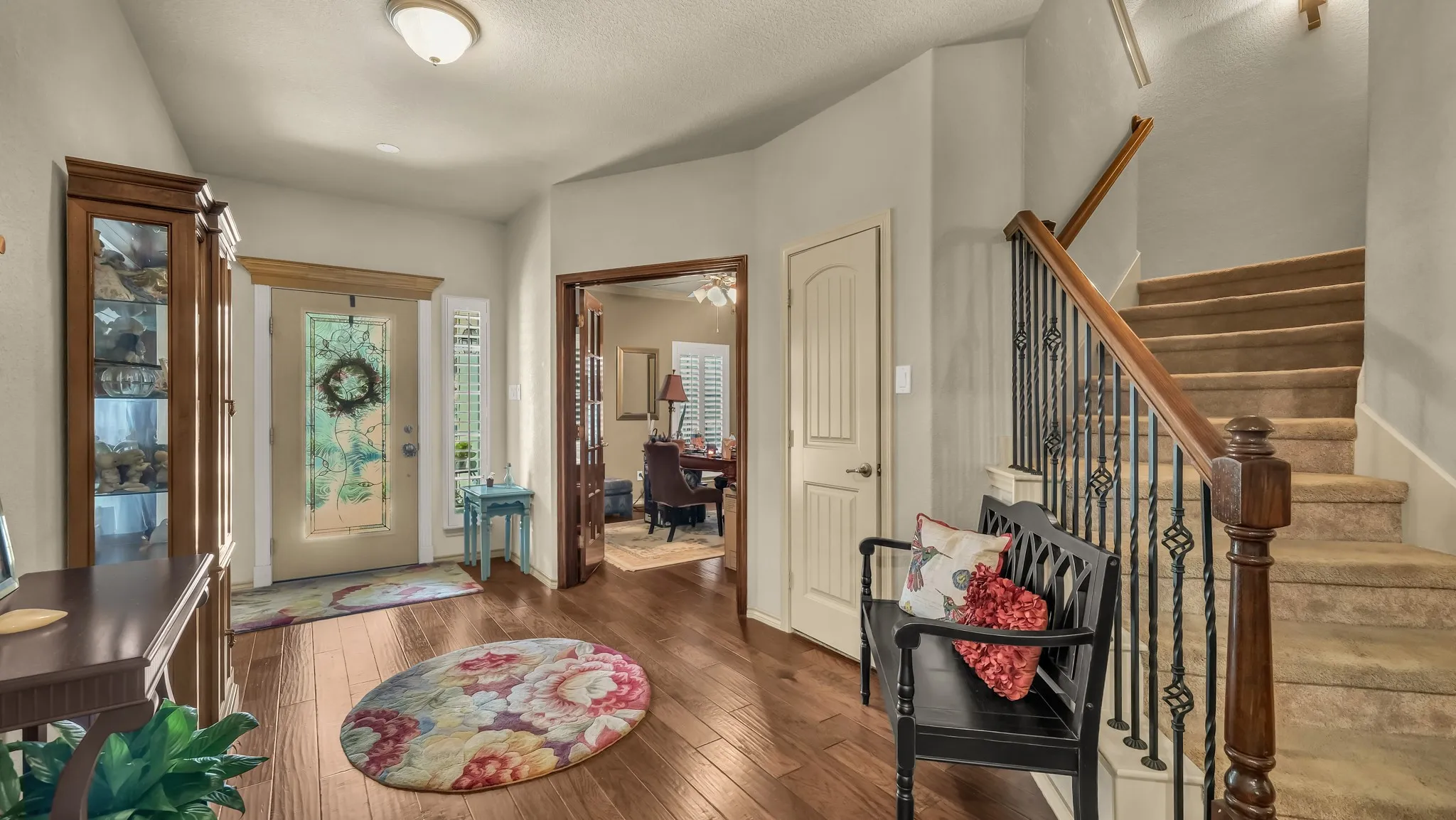 Foyer entry featuring wood-finish flooring, a decorative glass-paneled entry door, and a carpeted staircase with wrought iron balusters and a wood handrail