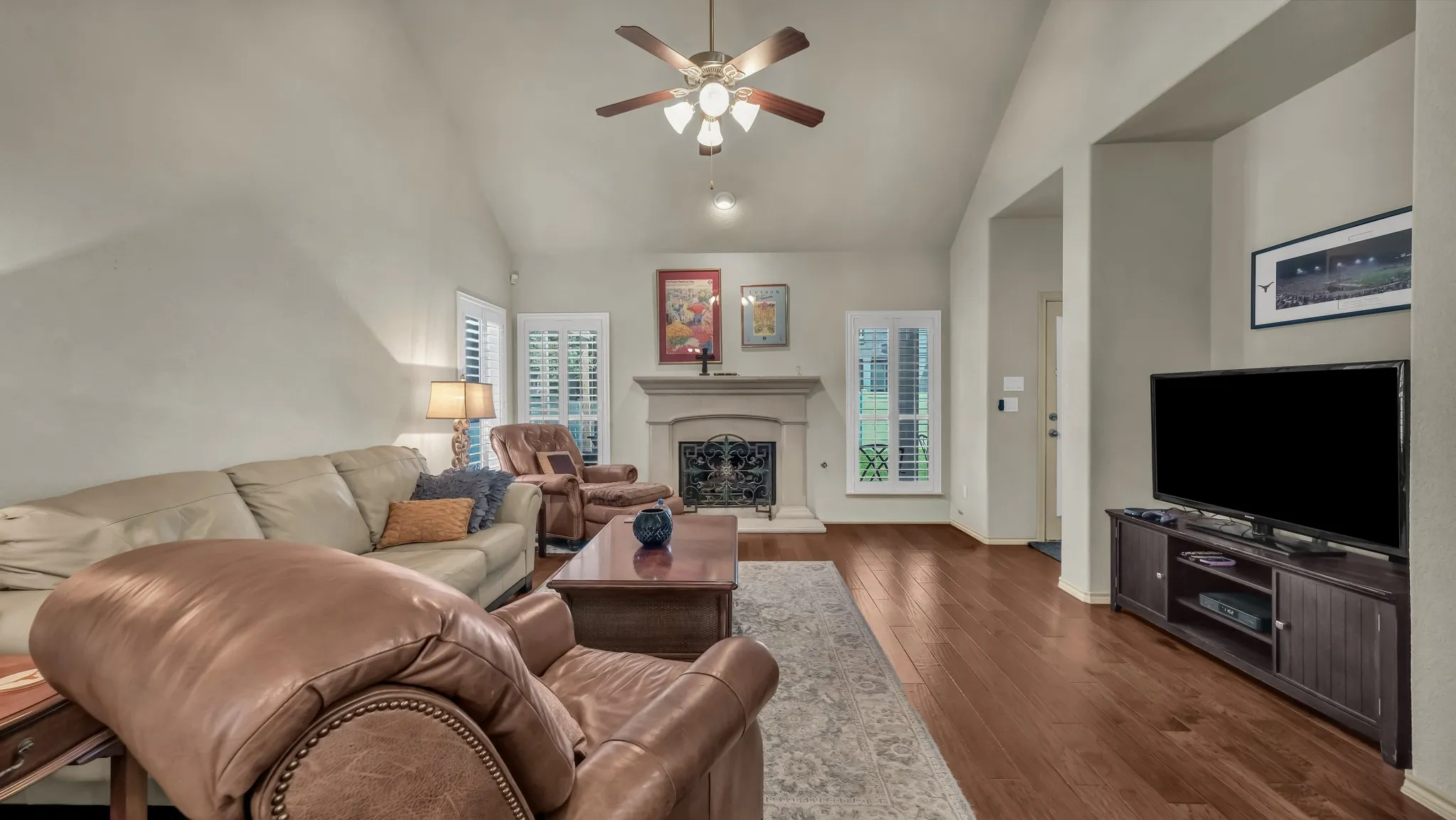 Spacious living area featuring vaulted ceilings, wood-finish flooring, and a central fireplace with a decorative mantel