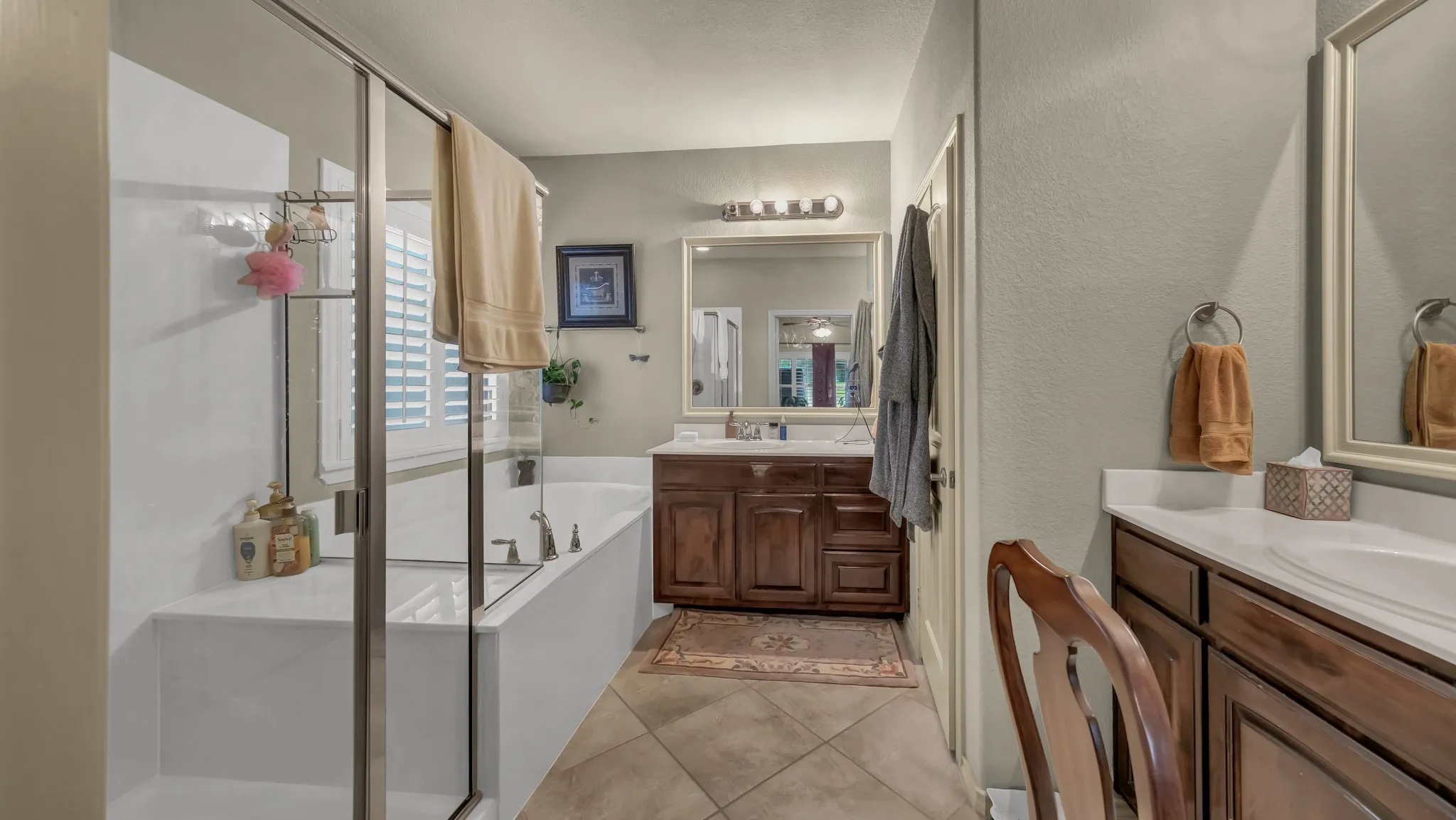 Bathroom featuring a large soaking tub with a shower enclosure, dual wood-finish vanity with integrated sinks, and tiled flooring