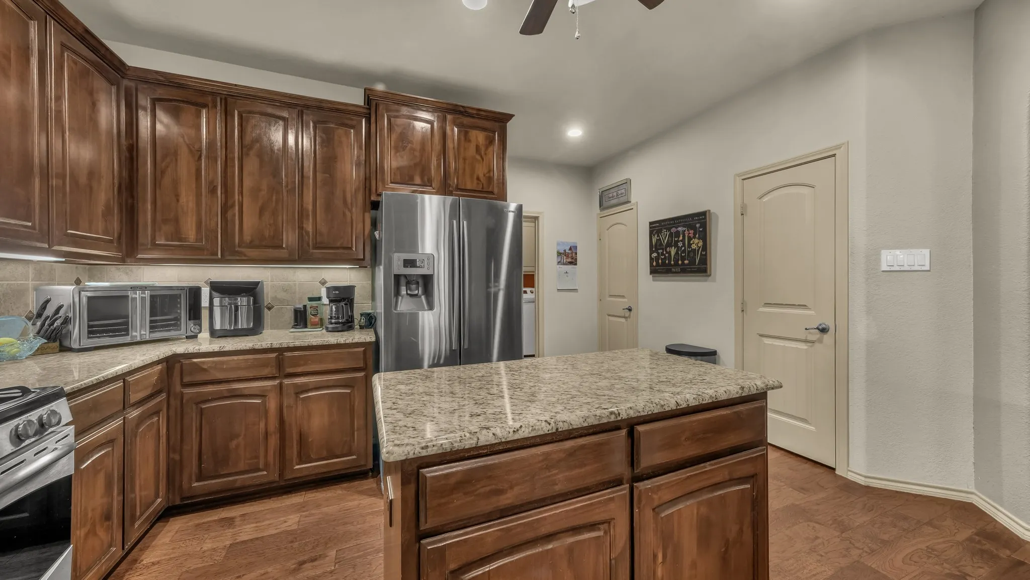 Kitchen featuring a central island with a granite countertop, extensive wood cabinetry, stainless steel refrigerator, and wood-finish flooring