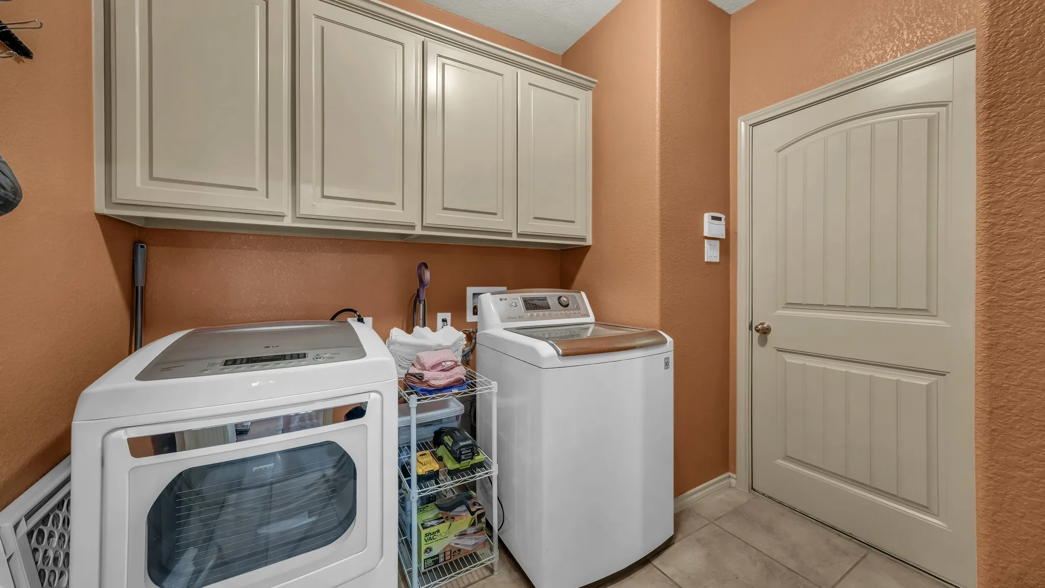 Utility room featuring upper cabinetry with panel doors, neutral wall paint, and tiled flooring