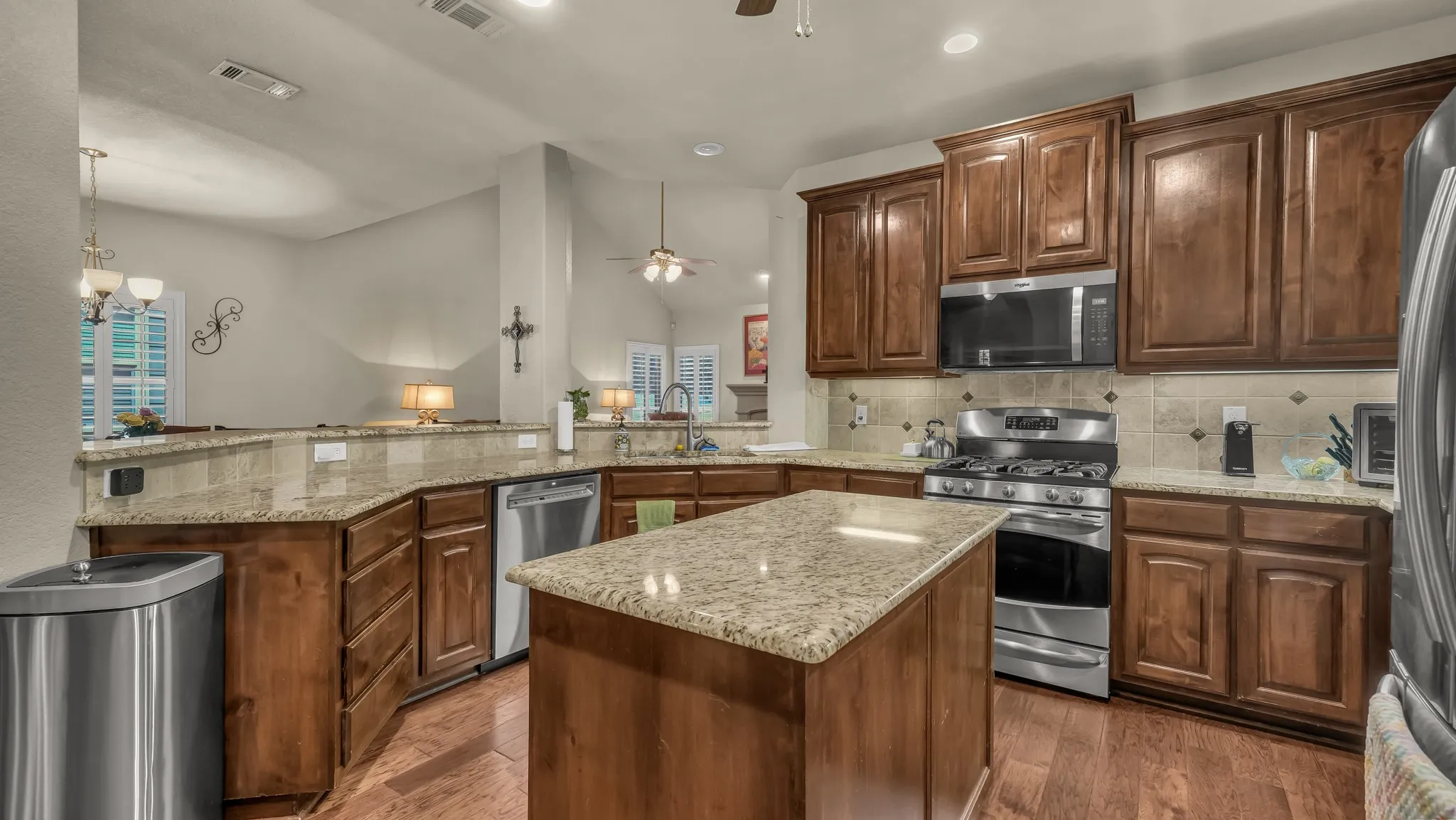 Kitchen featuring wood-finish flooring, granite countertops, wood cabinetry, stainless steel appliances, and a central island