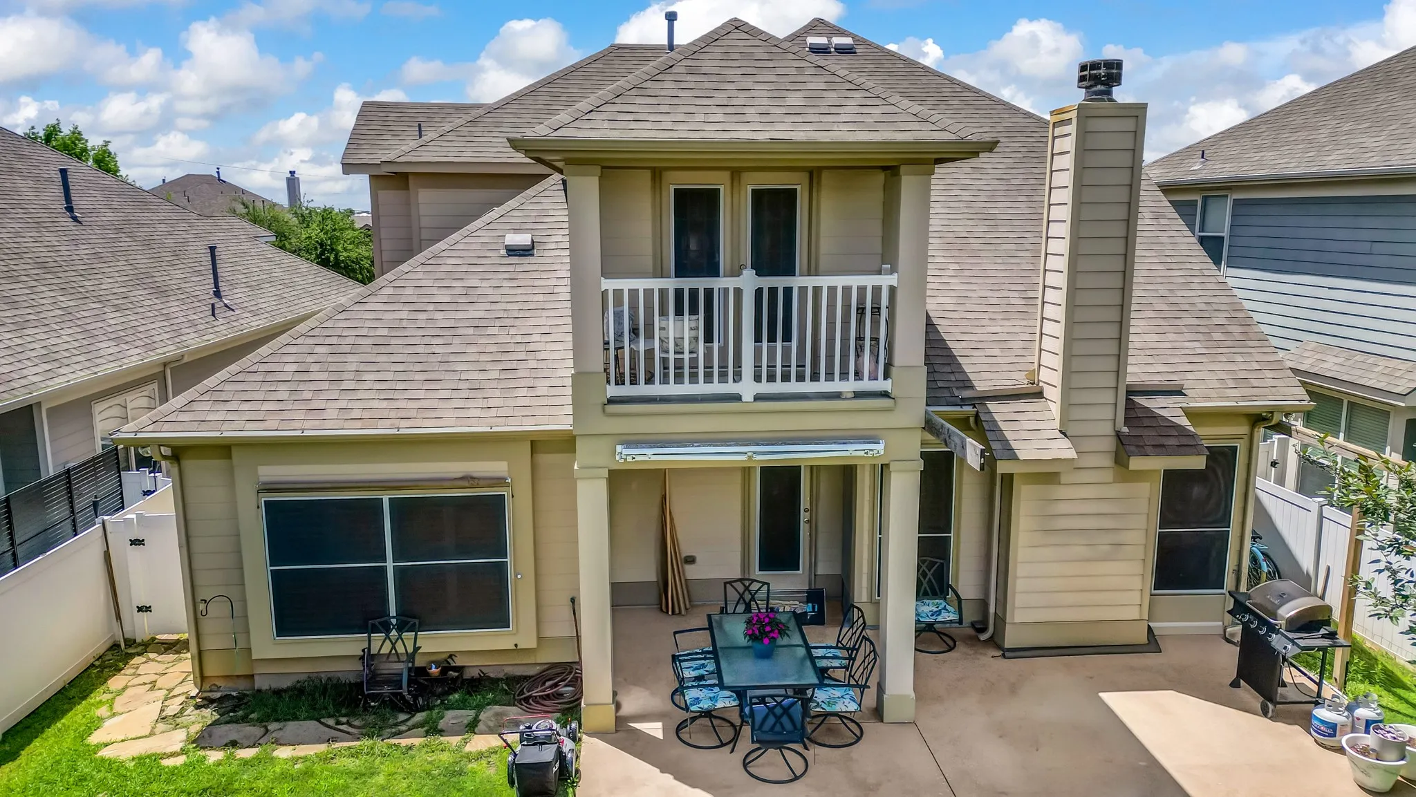 Two-story rear exterior featuring a covered patio, second-story balcony with white railing, and an exterior chimney