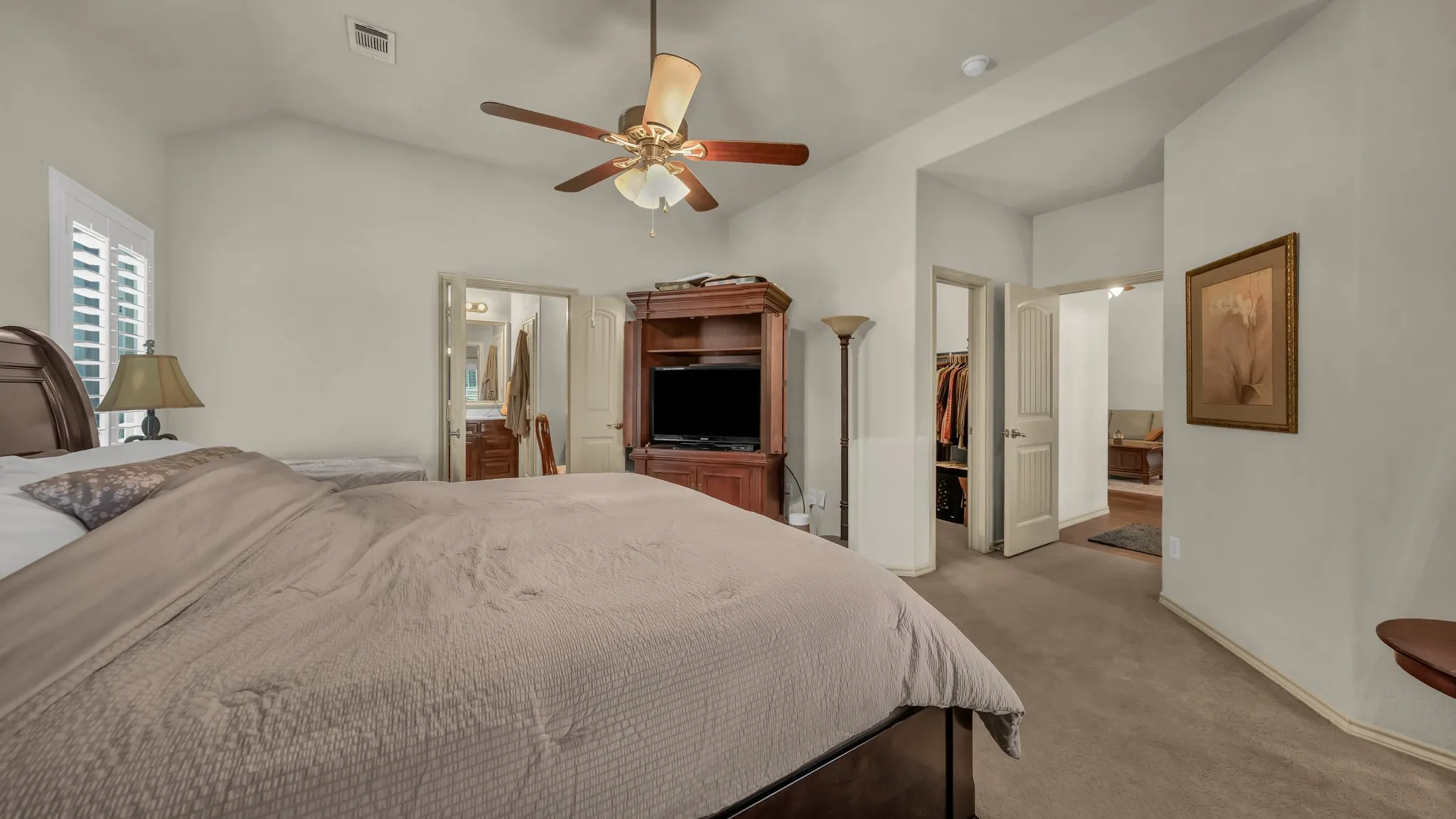 Vaulted ceiling with a ceiling fan, window with plantation shutters, wood-finish built-in cabinetry, and neutral carpeting