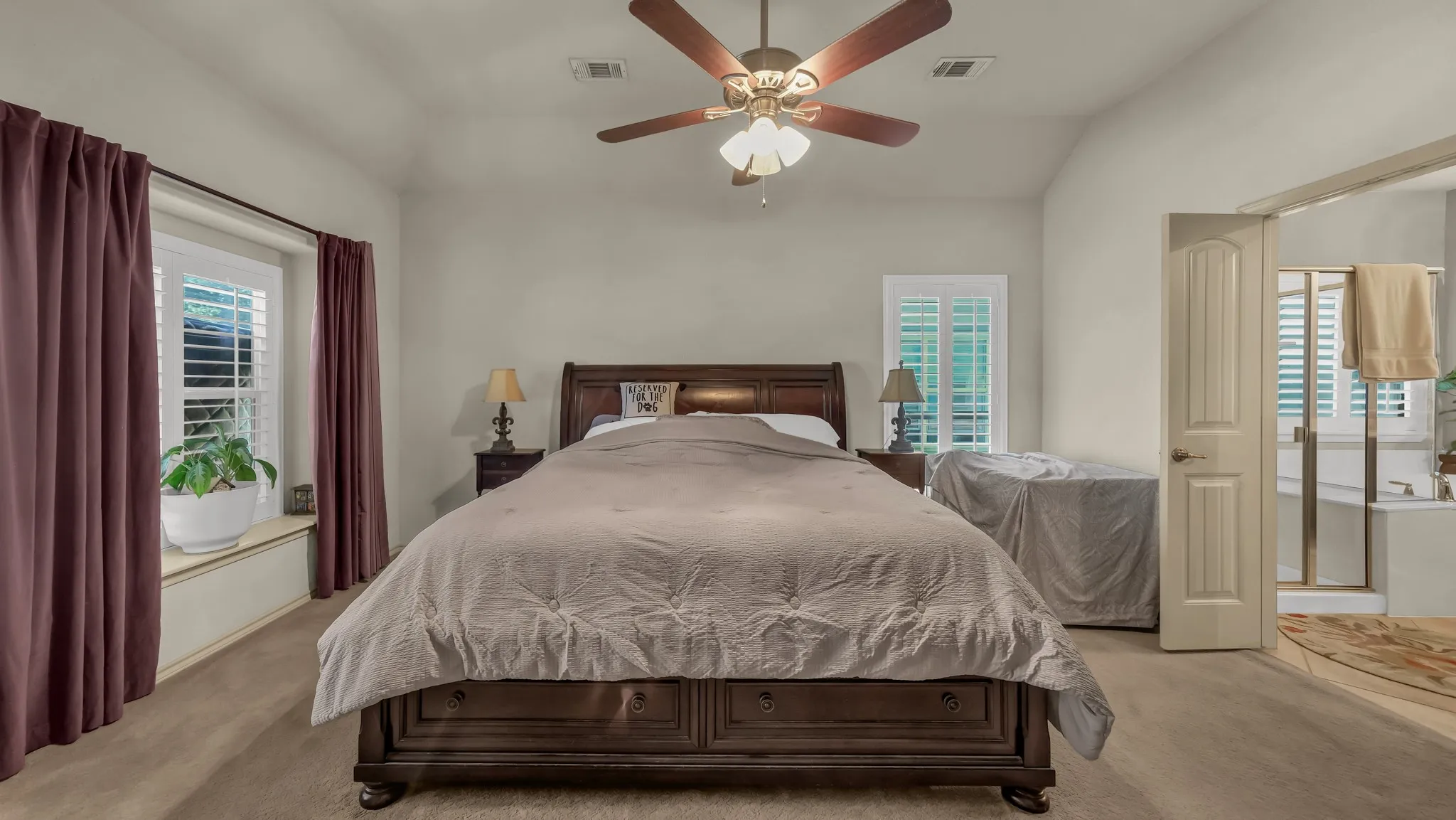 Carpeted bedroom featuring vaulted ceilings, a ceiling fan with integrated lighting, and plantation shutters on multiple windows