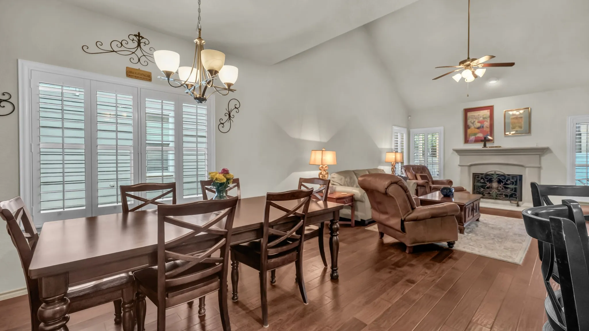 Open-concept living area featuring wood-finish flooring, a vaulted ceiling, and white plantation shutters