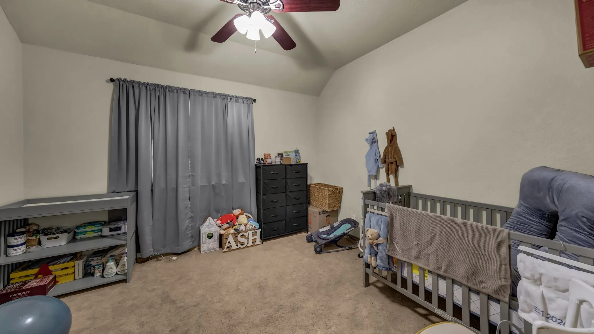 Carpeted room featuring a ceiling fan, window with drapes, and neutral wall paint