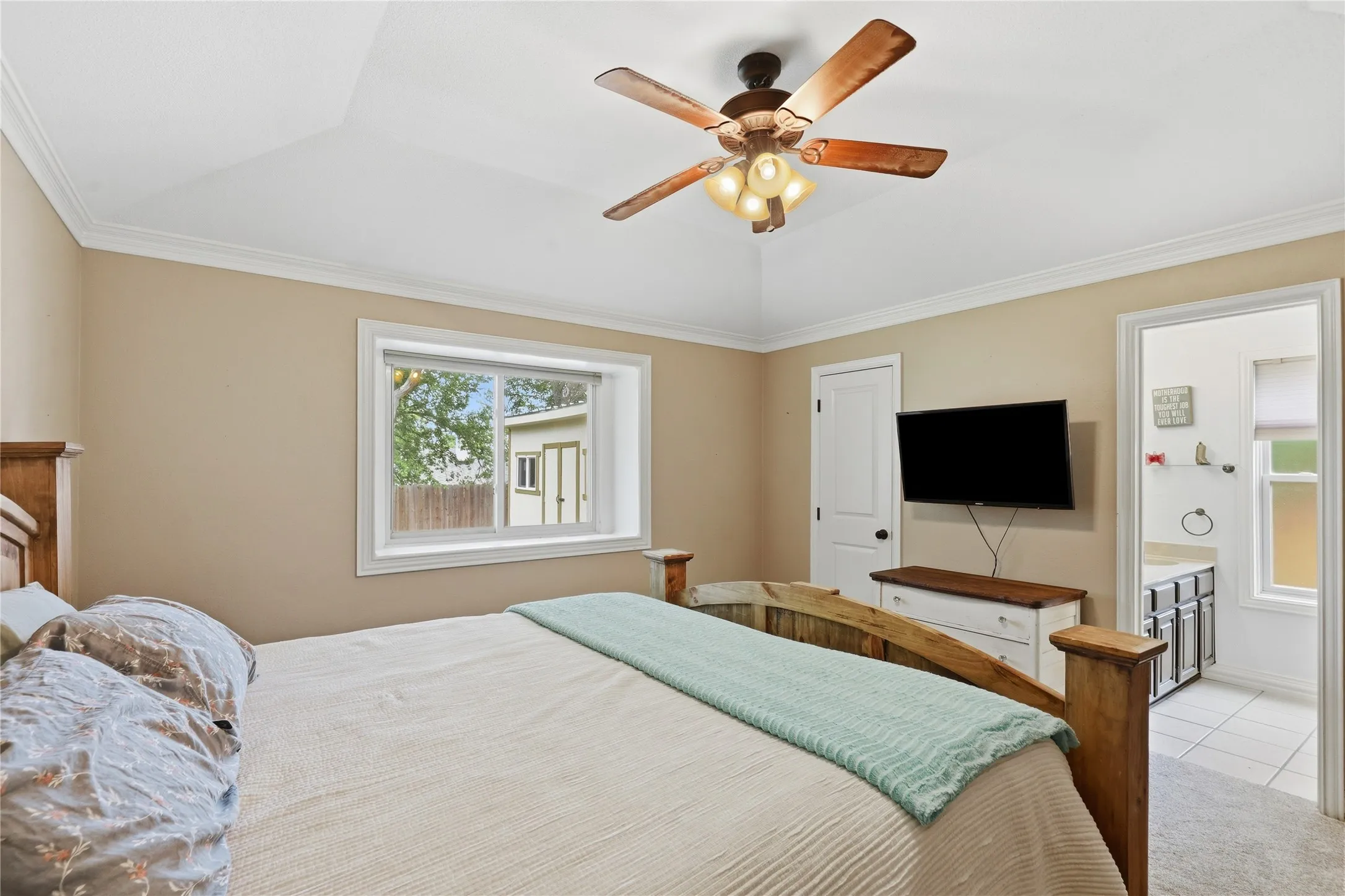 Carpeted bedroom featuring a tray ceiling with crown molding and a wood-finish ceiling fan