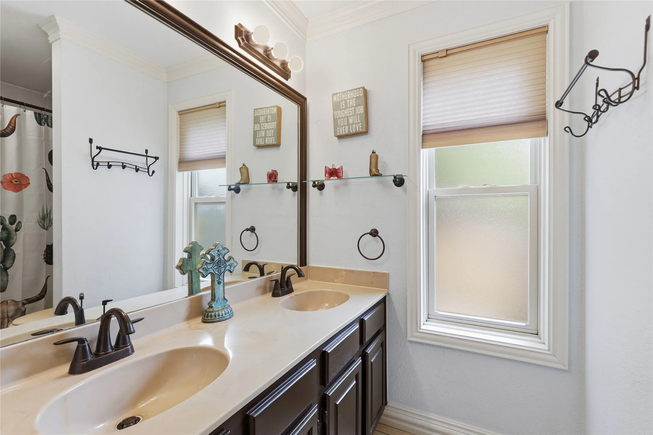 Double vanity with integrated sinks, oil-rubbed bronze fixtures, a framed mirror, and a privacy window featuring a cellular shade