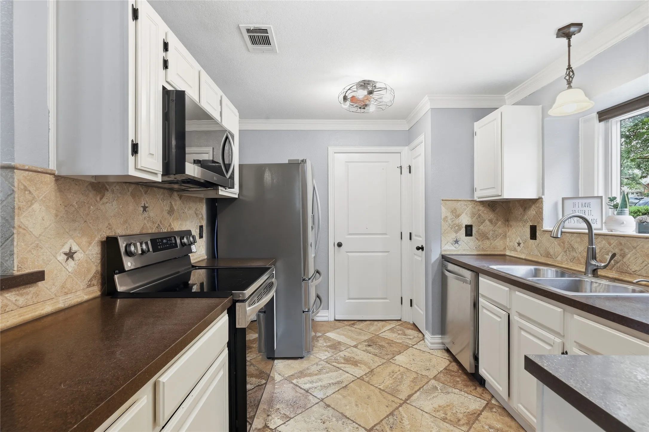 Kitchen featuring light wood-finish cabinetry, dark countertops, and a tiled backsplash