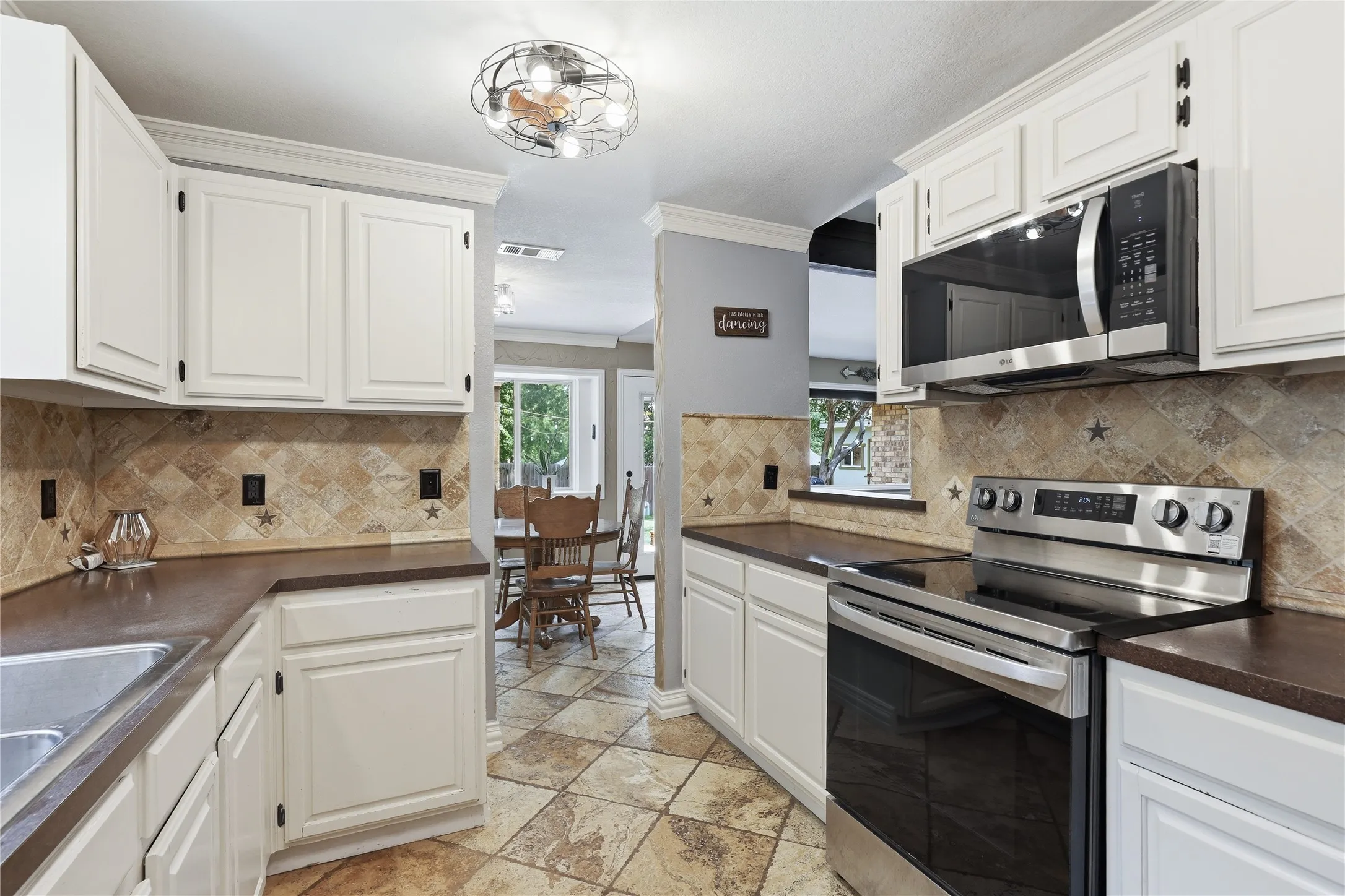 Kitchen featuring white cabinetry, dark countertops, a patterned tile backsplash, stainless steel appliances, and tile flooring