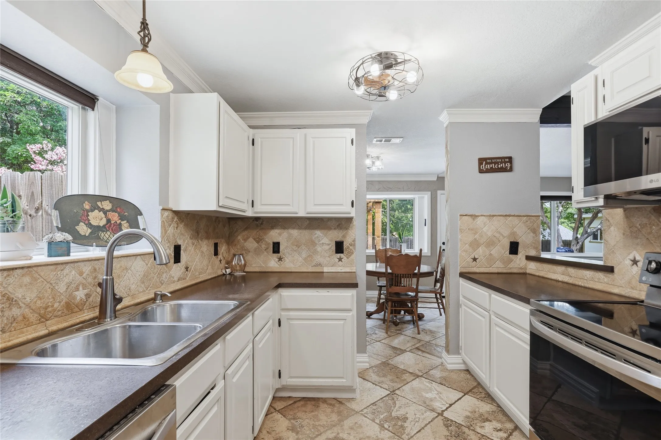 Kitchen featuring white cabinetry, dark countertops, a double basin stainless steel sink, and a tiled backsplash