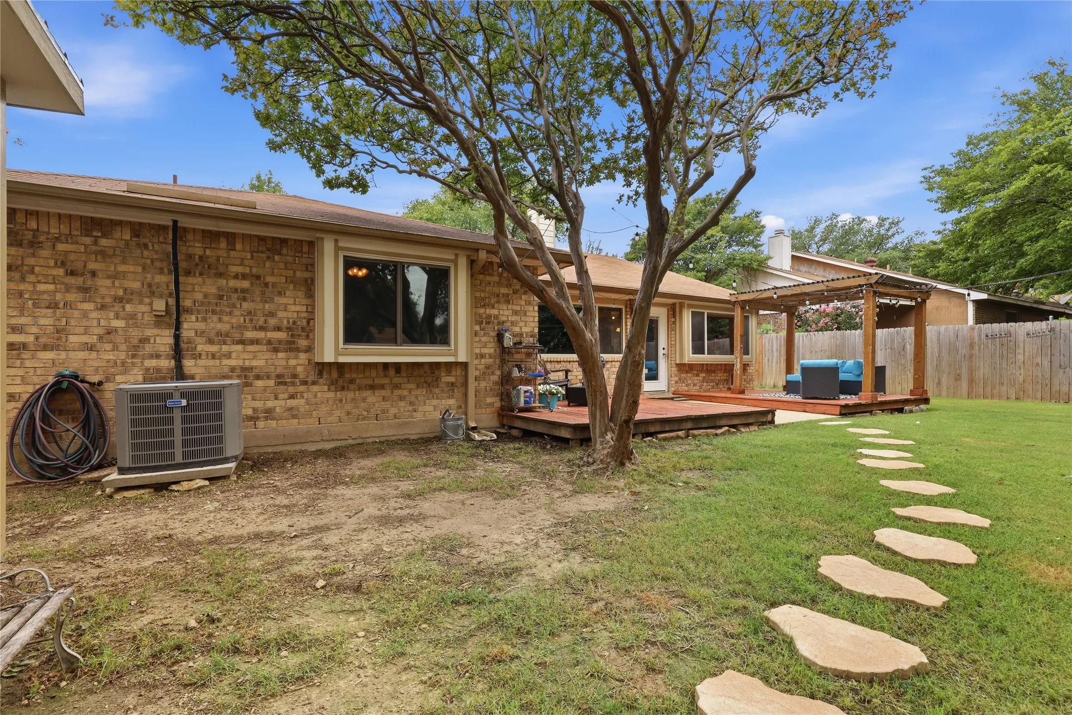 Expansive backyard featuring a stone paver path, mature tree, and a wooden deck