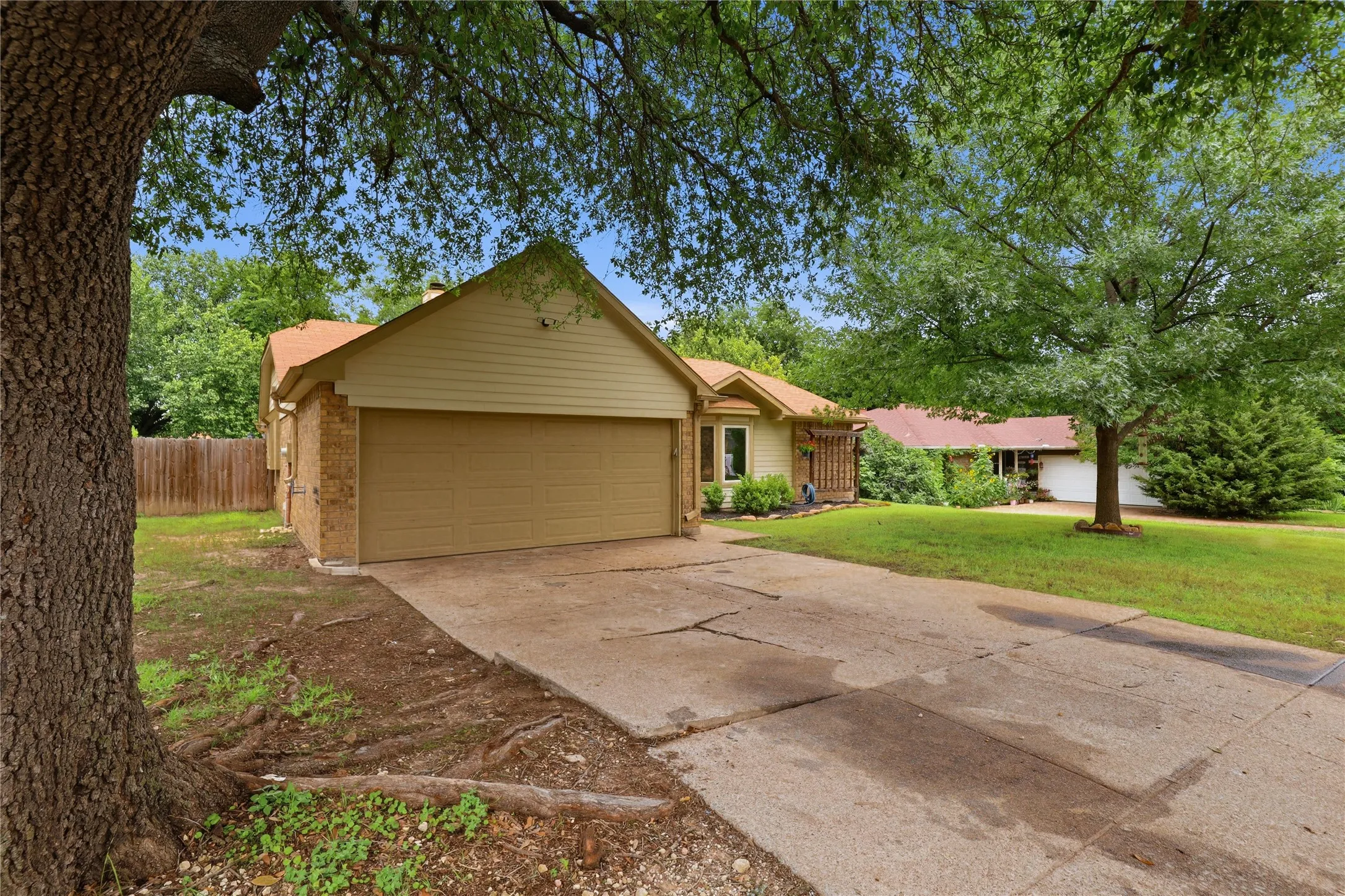 Front exterior featuring a two-car garage, brick facade, light-toned siding, a concrete driveway, and mature trees