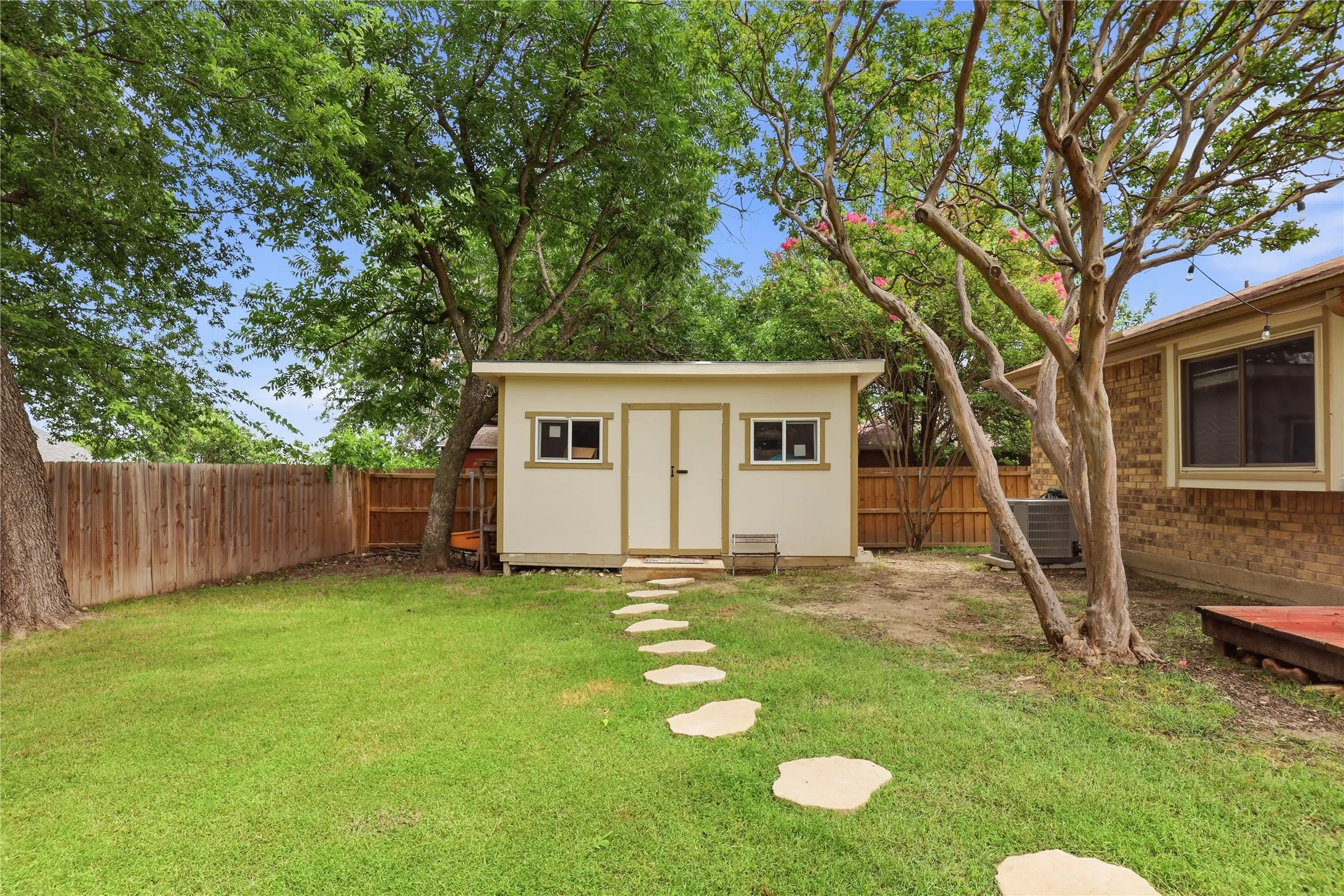 Spacious backyard featuring a storage shed with dual doors and two windows, a flagstone pathway, and mature trees providing natural shade