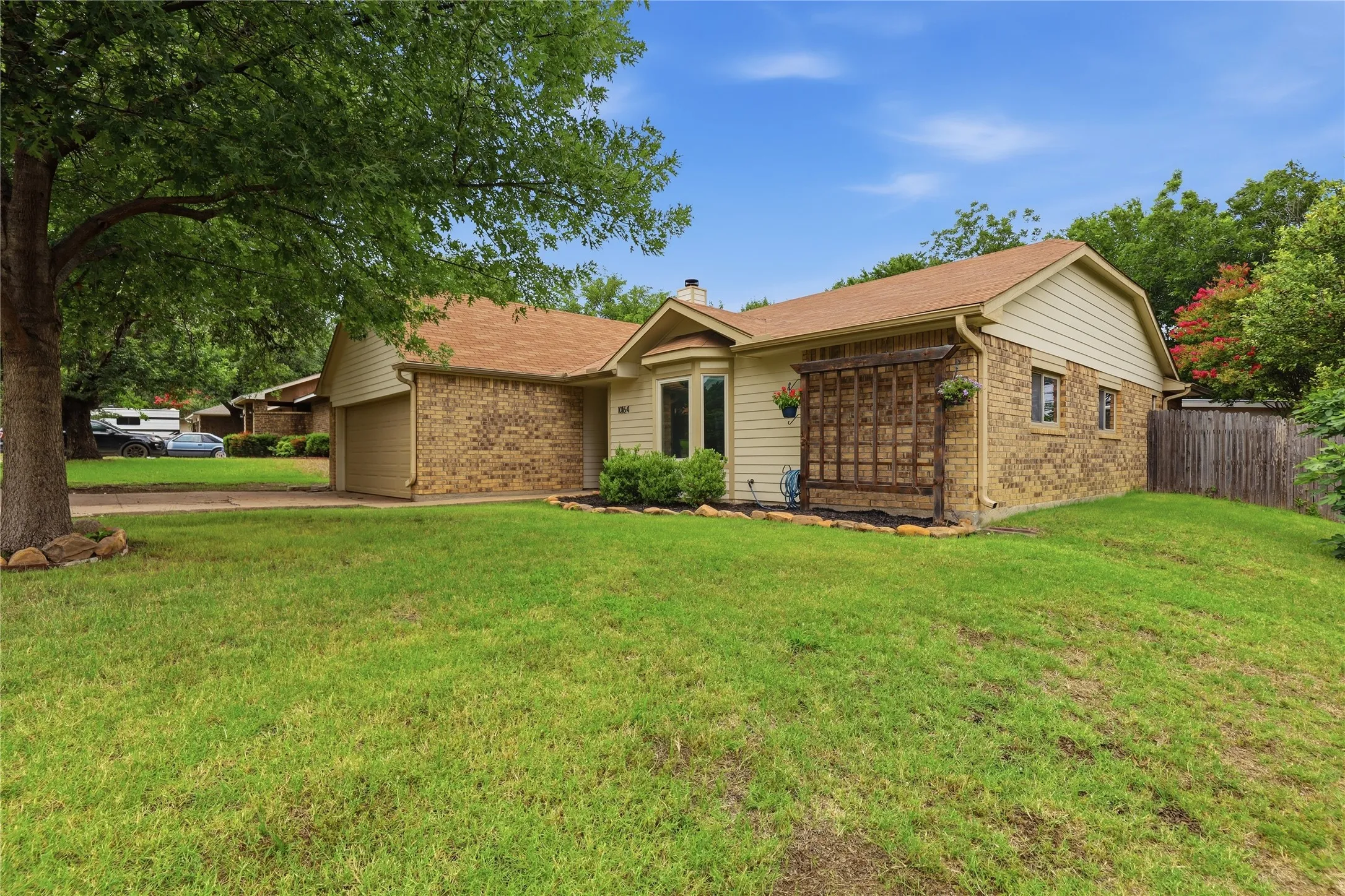 Single-story residence featuring a brick and siding exterior, a prominent bay window, an attached garage, a wooden trellis accent, and a fenced side yard