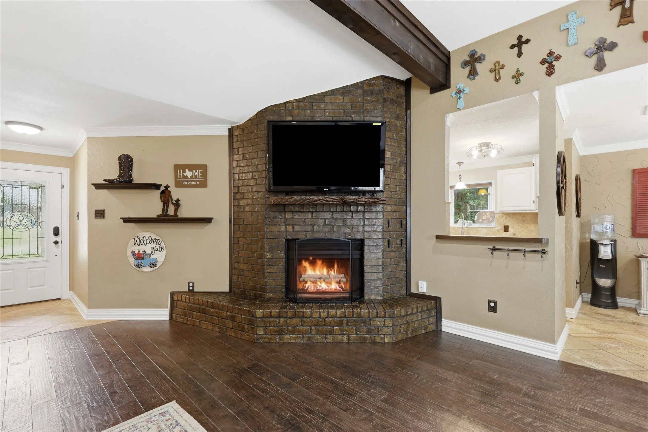 Living area featuring an angular brick fireplace, wood-finish flooring, and a pass-through window to the kitchen