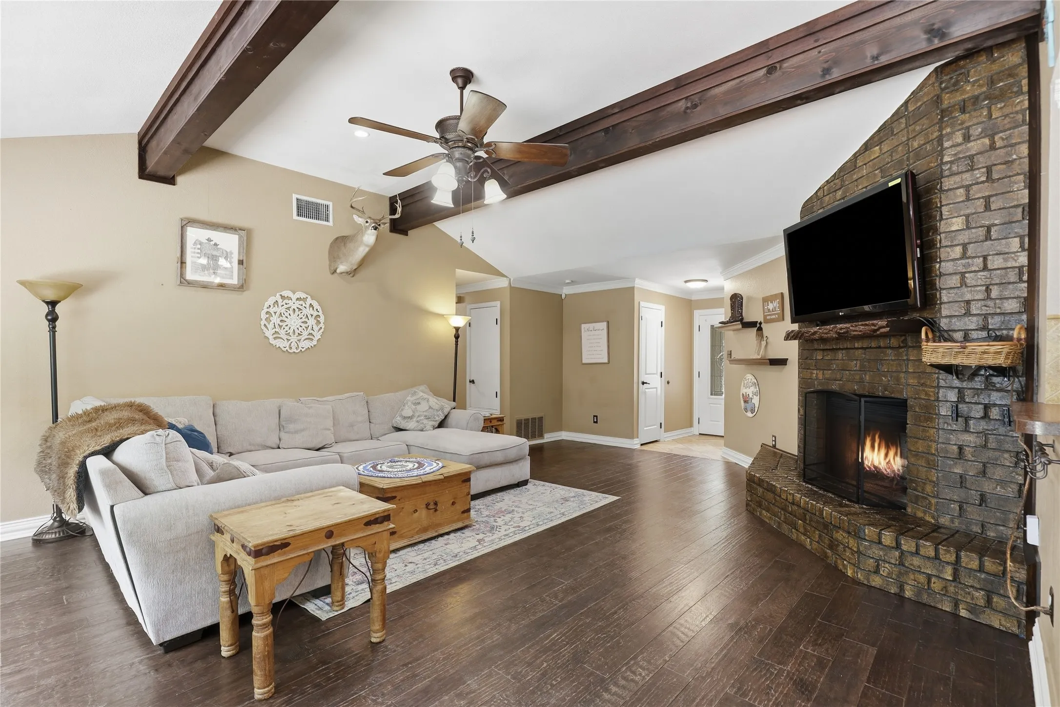 Spacious living area featuring a brick fireplace, dark wood-finish flooring, and exposed ceiling beams