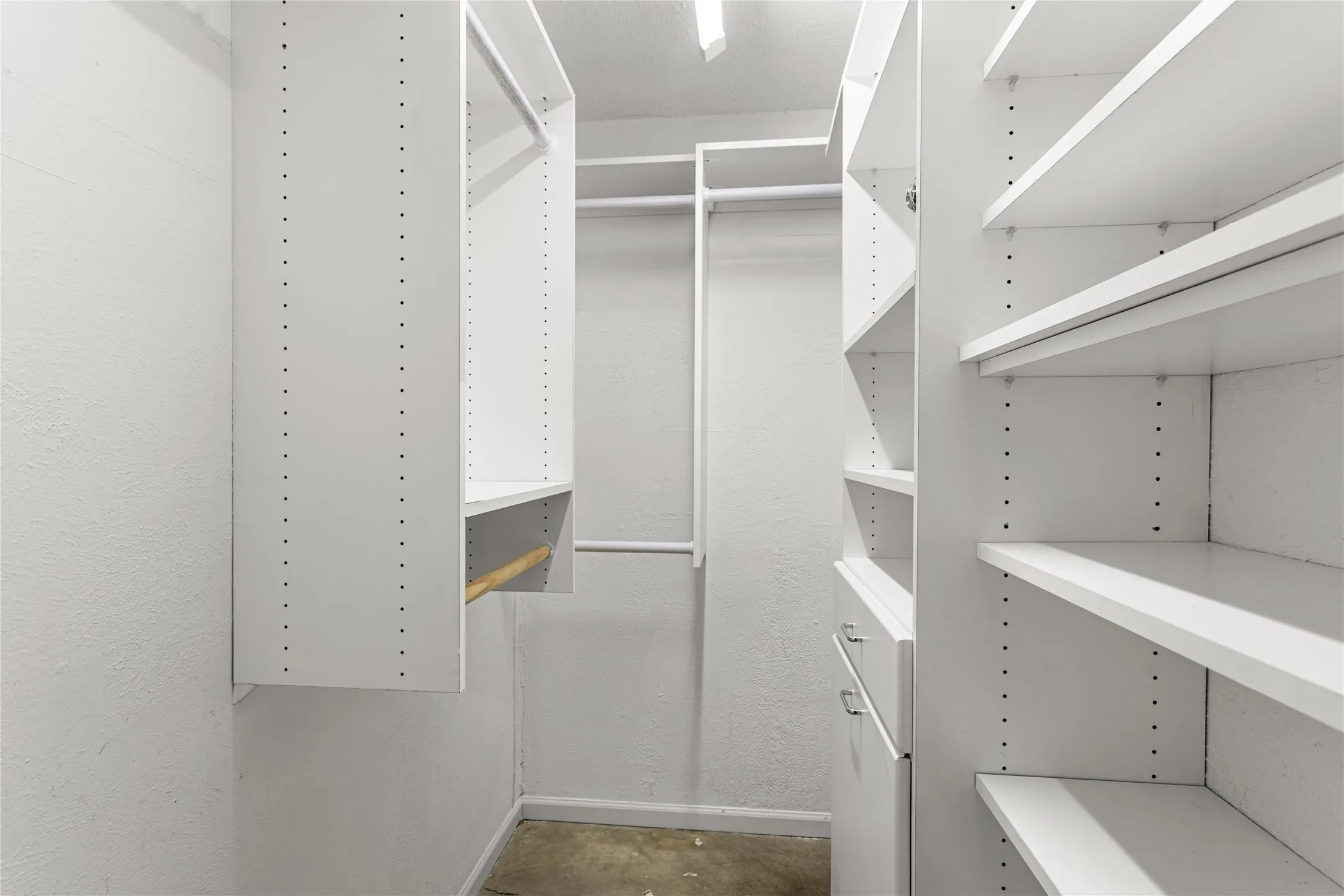 Walk-in closet featuring white built-in shelving, multiple hanging rods, and a lower built-in drawer unit