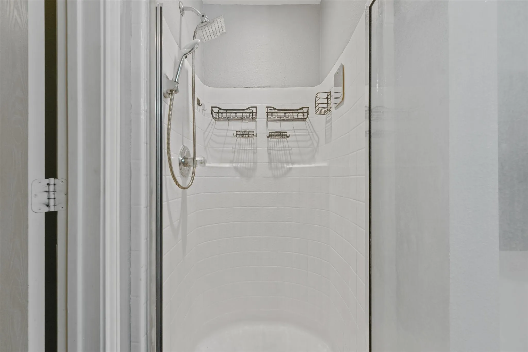 Tiled shower enclosure featuring a handheld showerhead, wall-mounted shower caddy, and clear glass door