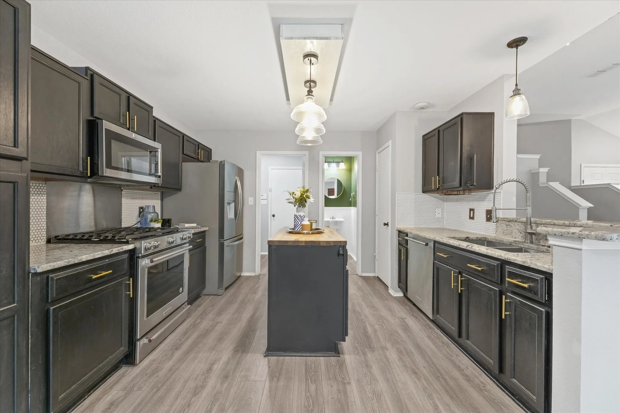 Modern kitchen featuring dark cabinetry, stainless steel appliances, light granite countertops, a central island with a wood-finish top, and wood-finish flooring