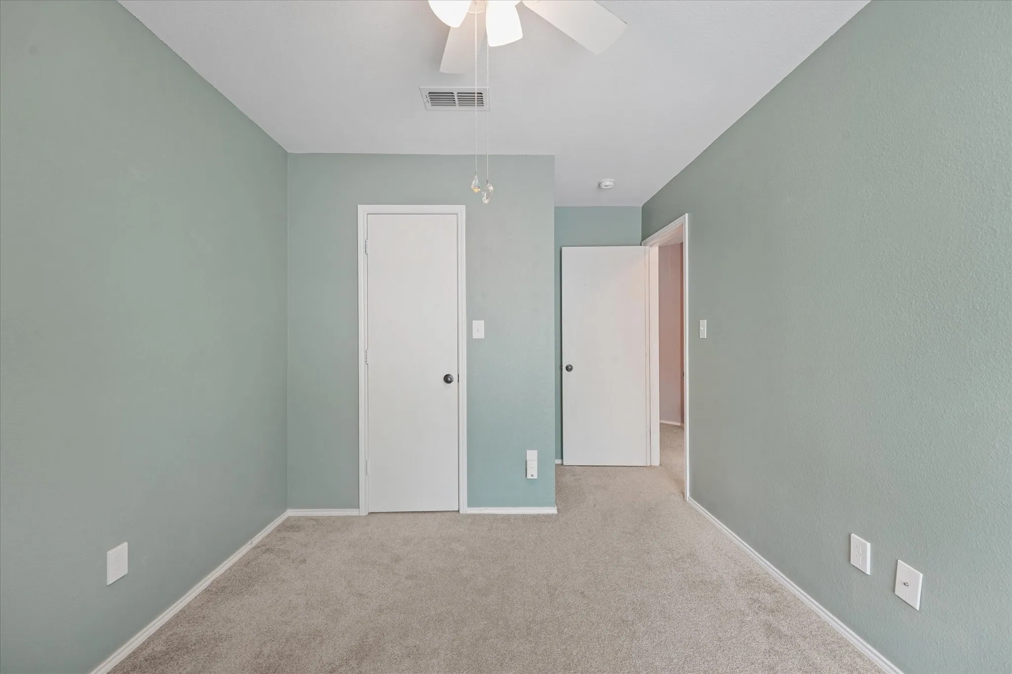 Interior room featuring light green walls, light-colored carpet, white baseboards, and a ceiling fan with light fixture