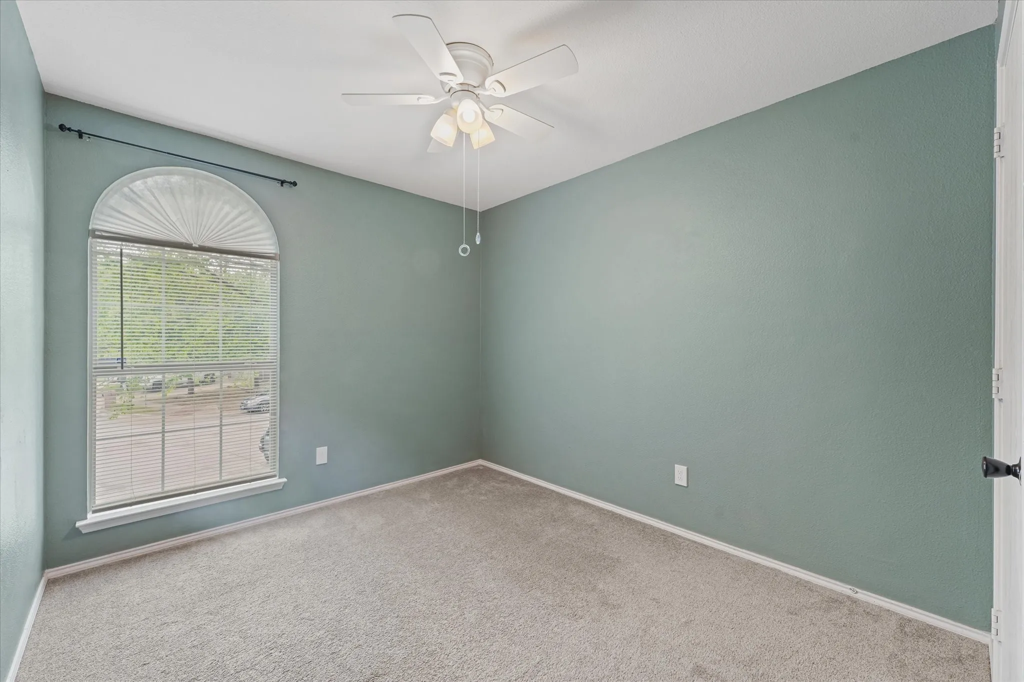 Room featuring an arched window with blinds, light green walls, a neutral carpet, and a ceiling fan with integrated lighting